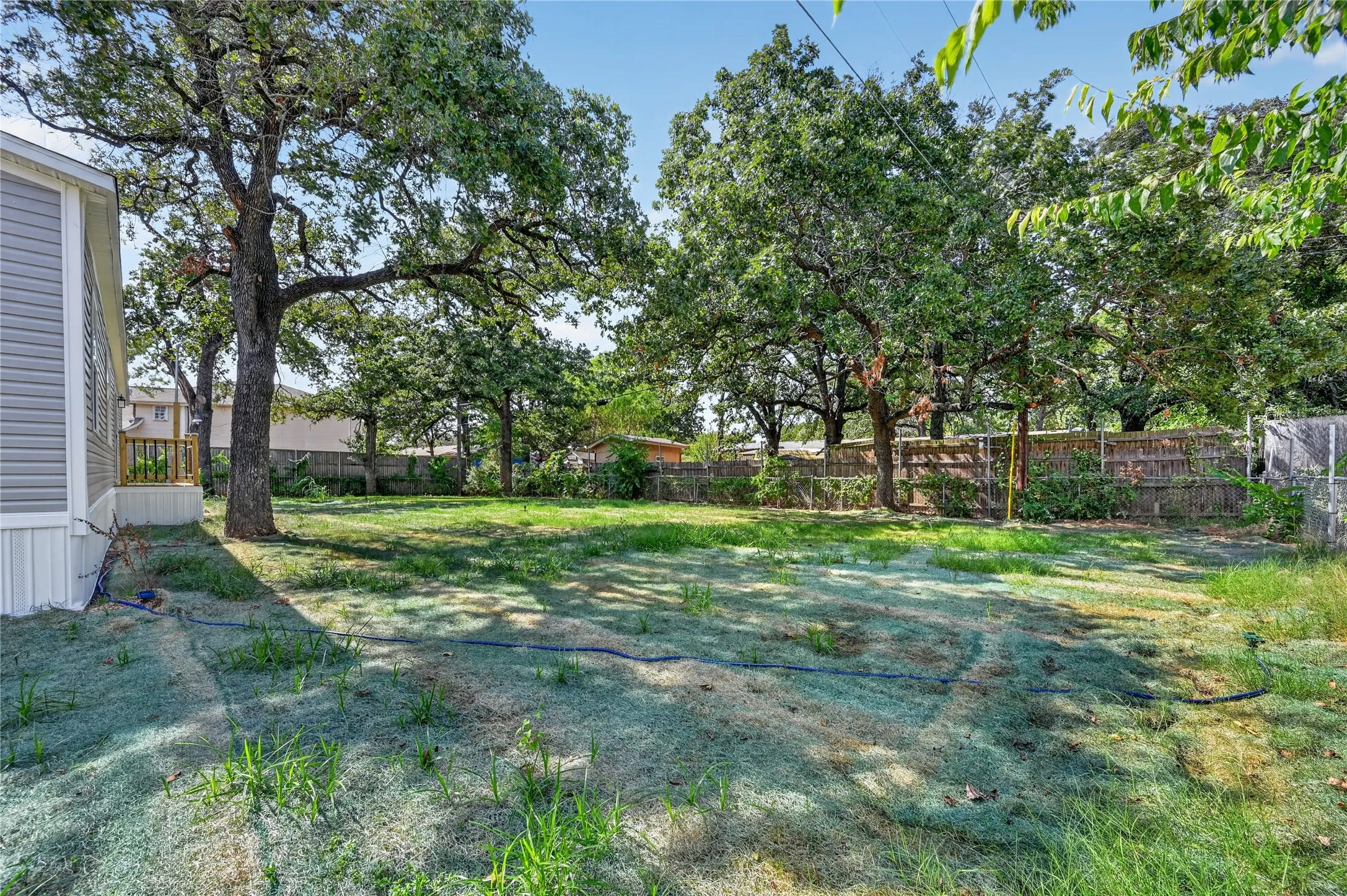 Expansive rear yard featuring mature trees, a wood privacy fence, and a side deck with wooden railings
