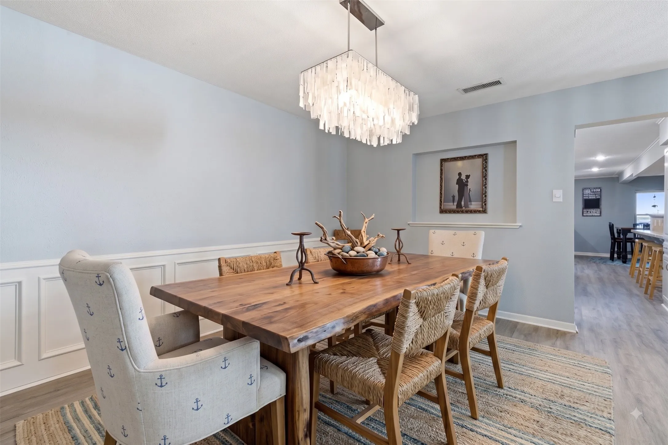 Dining area with a rectangular wood table, wainscoting, and a linear pendant light fixture