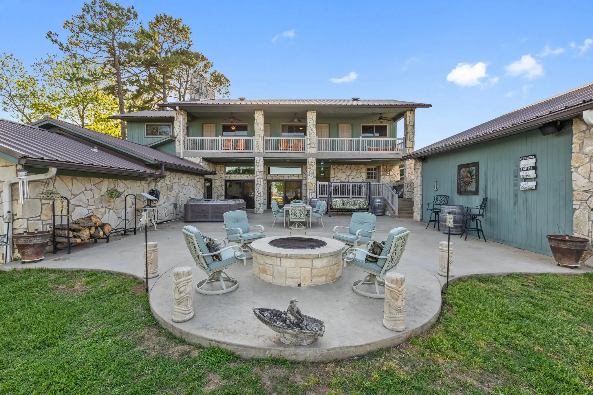 Expansive concrete patio featuring a built-in stone fire pit, a hot tub, and a two-story exterior with stone and siding finishes