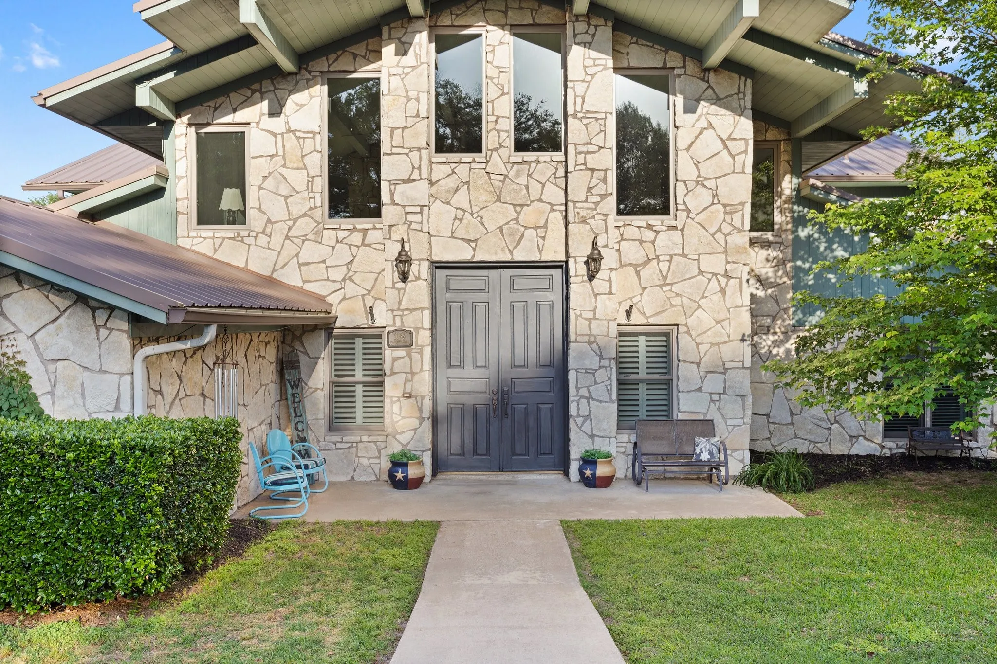 Stone veneer exterior with multiple window styles, prominent double entry doors, and a metal roof
