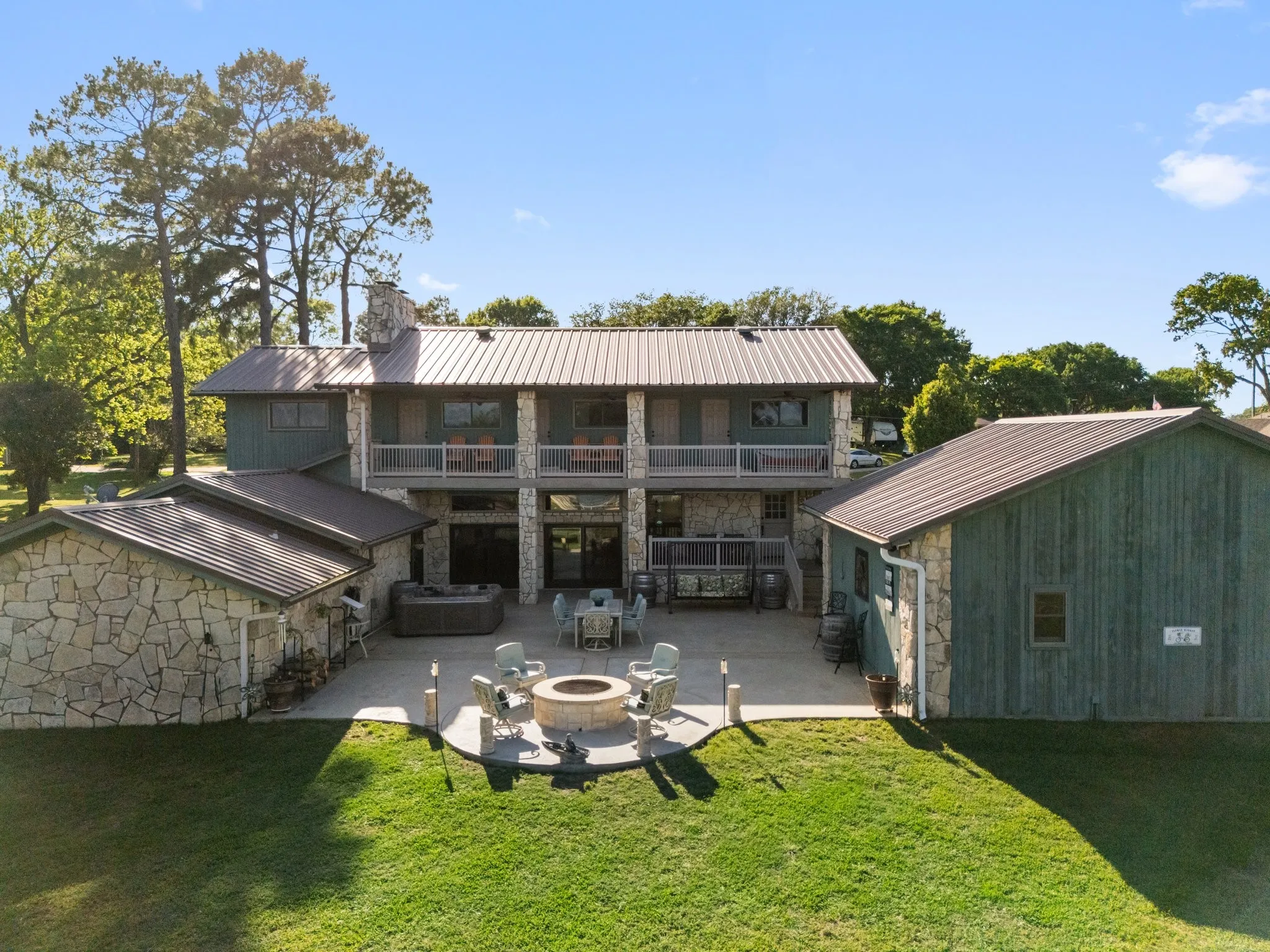 Exterior featuring stone and board-and-batten siding, multiple balconies, a lower-level patio with a built-in fire pit, and a metal roof