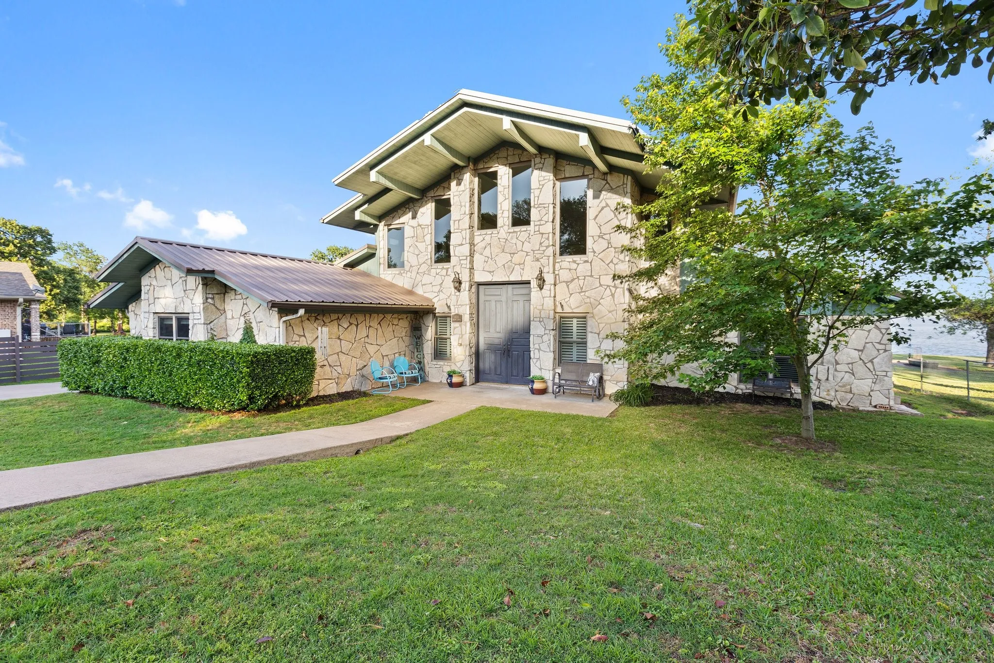 Stone facade, multi-level roofline, prominent entryway, mature landscaping, and waterfront access