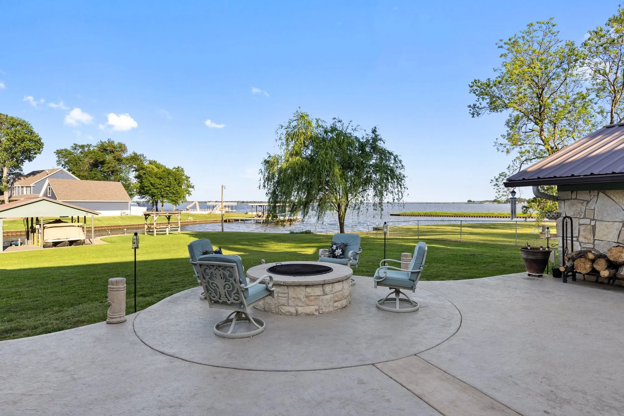 Stamped concrete patio with a stone fire pit, extensive green lawn, and waterfront access featuring a boat dock