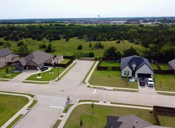Aerial view showcasing a new construction home with modern architectural design, situated on a spacious manicured lot with mature landscaping