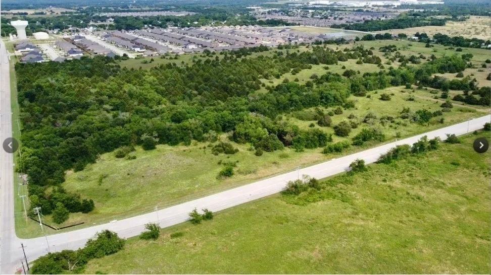 Expansive undeveloped land with mature trees and open grassy areas, bordered by a paved road