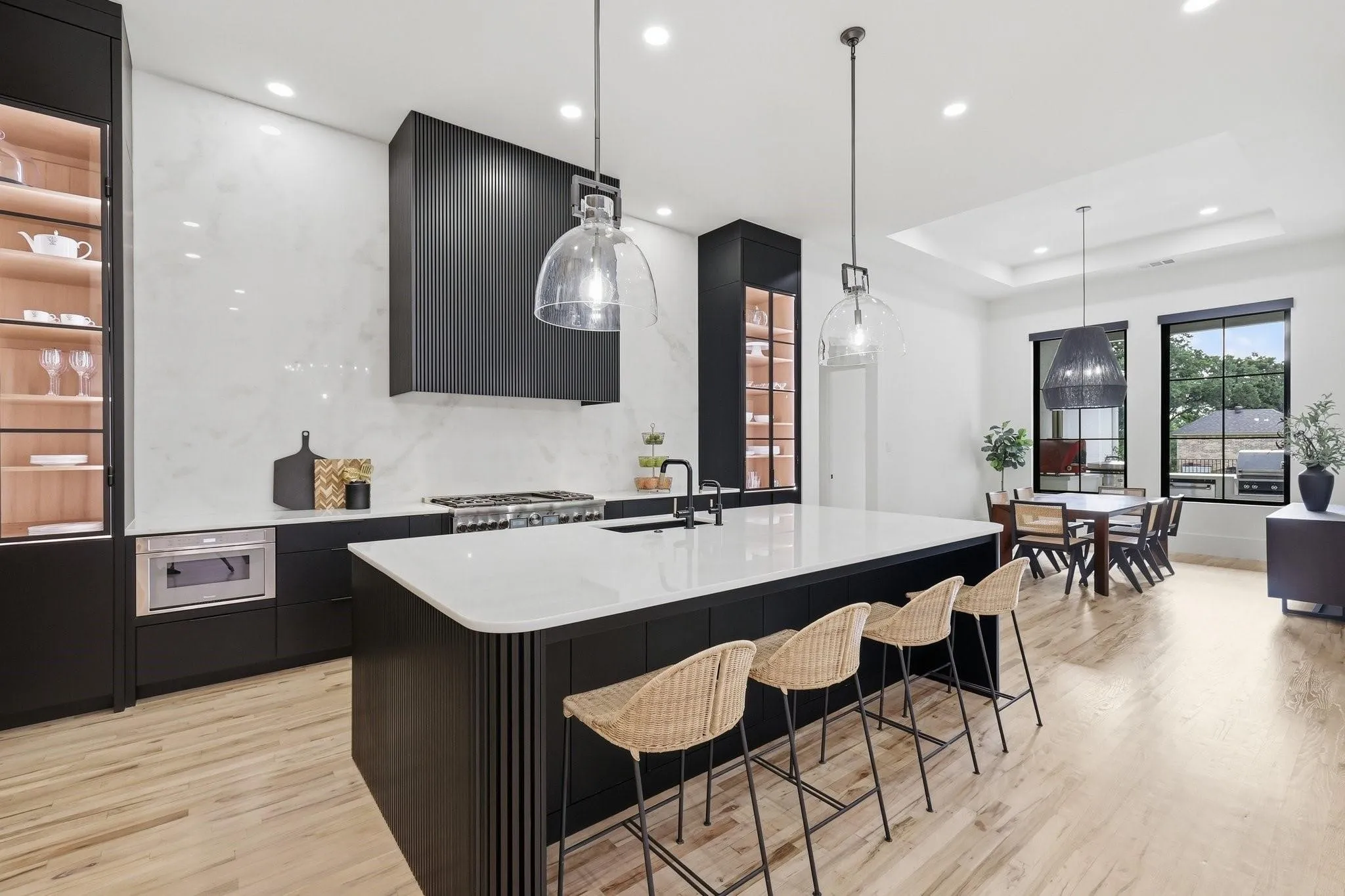 This stunning Kitchen showcases Bianco Rhino sealed marble countertops, illuminated glass display built-ins with custom iron doors, and the highest level of custom inset cabinetry featuring soft-close doors and drawers. Thoughtfully crafted with a blend of rift-cut white oak, walnut, and painted finishes, the space is complemented by designer custom hardware, dramatic fluted millwork details, and premium luxury finishes throughout.