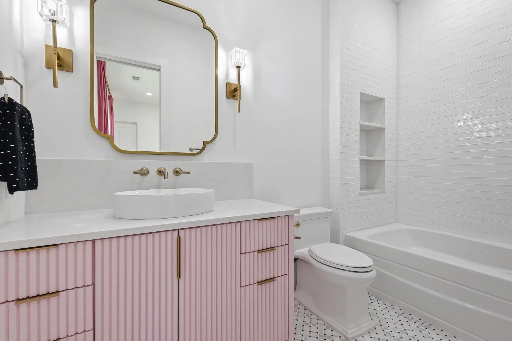 A private, designer-inspired Ensuite Bath showcasing a custom blush pink fluted vanity topped with a vessel sink, Restoration Hardware sconces and mirror, and timeless mosaic marble tile flooring.