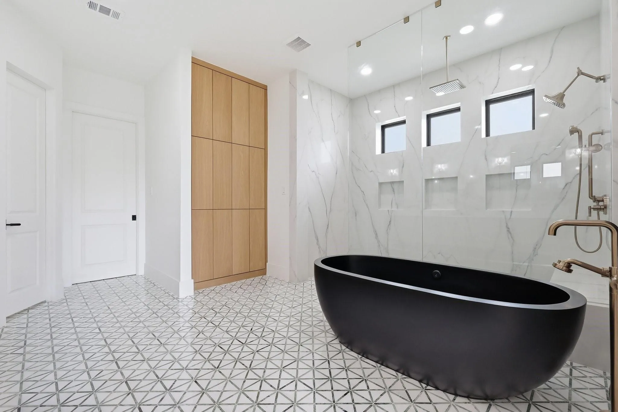 Spa-inspired design showcases a freestanding matte black concrete soaking tub, an oversized walk-in shower wrapped in large-format marble tile with a 2 cm single-slab quartz surround, and custom floor-to-ceiling wood cabinetry.
