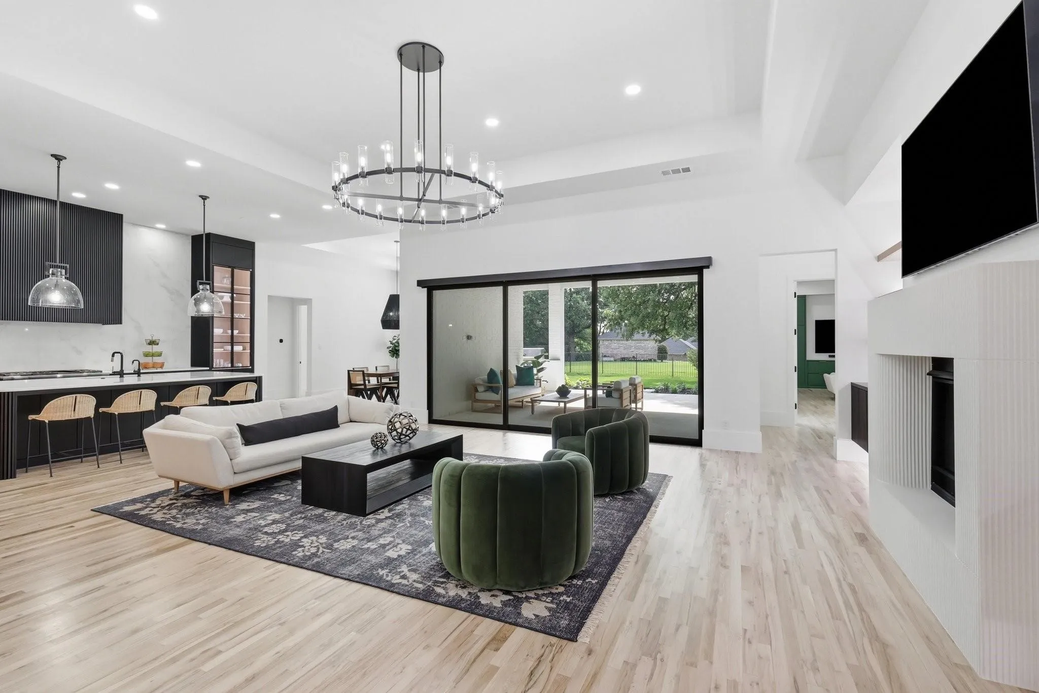 The expansive Living Room showcases a custom fluted stone fireplace surround, sliding glass doors with custom motorized shades (integrated wired), a statement Restoration Hardware chandelier, and abundant recessed lighting, creating a bright and inviting atmosphere.
