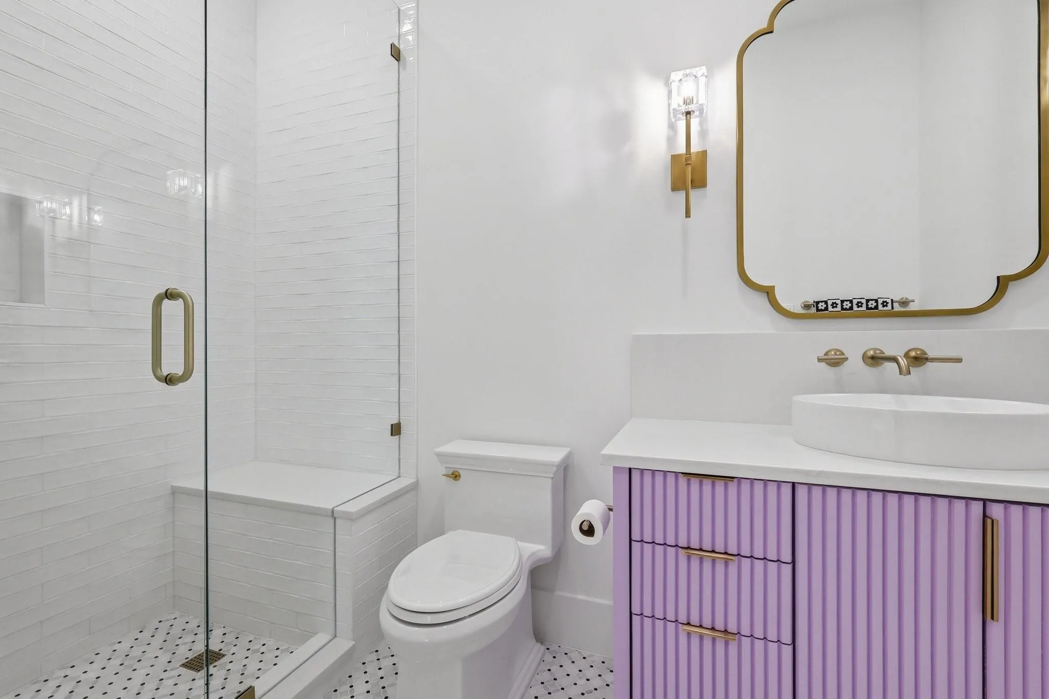 his private ensuite bath showcases a custom fluted lavender vanity topped with a vessel sink, designer Brizo brass hardware, Restoration Hardware mirror and sconces, and marble tile flooring.