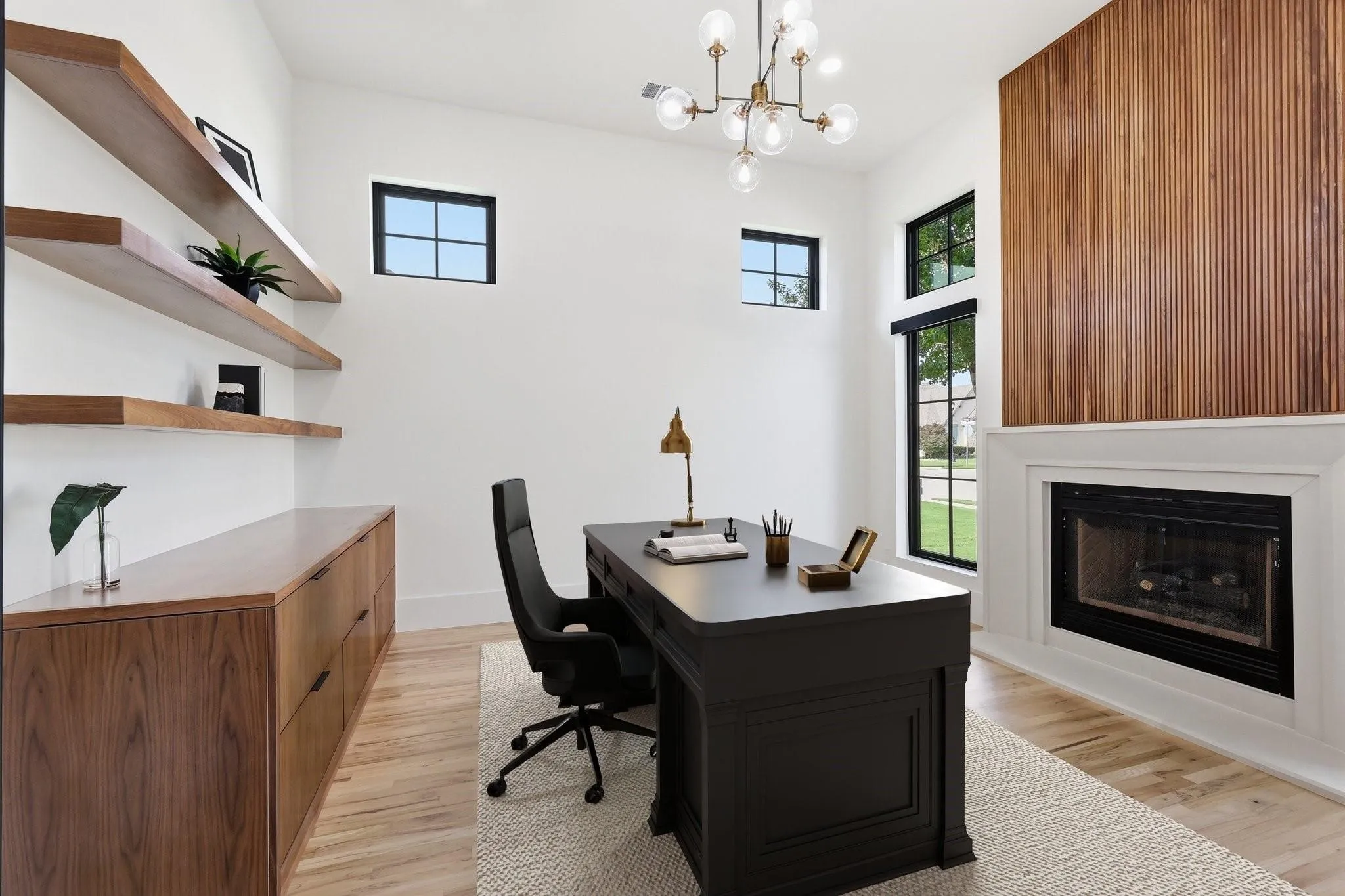 The Executive Office is highlighted by a stunning floor-to-ceiling linear fireplace with a wood accent wall, custom cast stone surround, custom iron doors, and custom built-in cabinetry with floating wood shelving.

