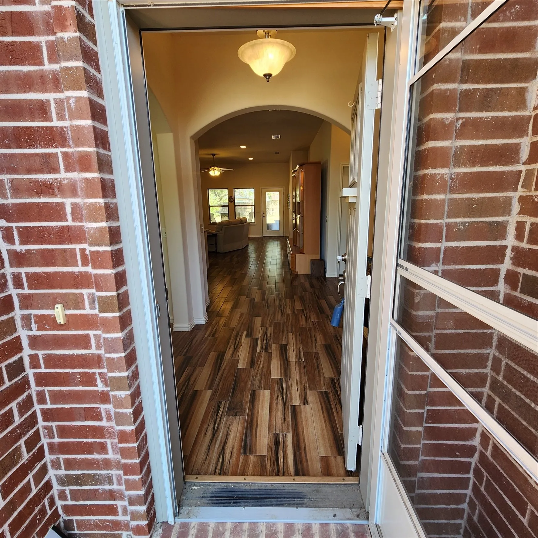 Brick exterior entry with an arched interior doorway, wood-finish flooring, and recessed lighting