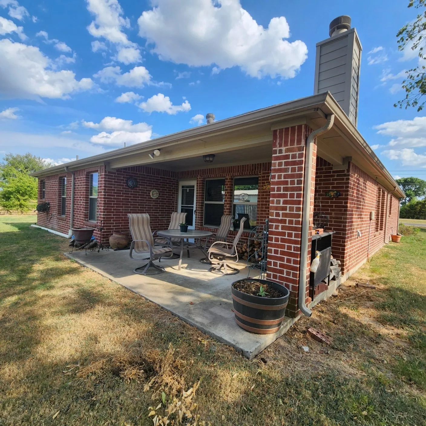 Brick exterior construction with a covered patio, concrete slab, and a prominent chimney structure