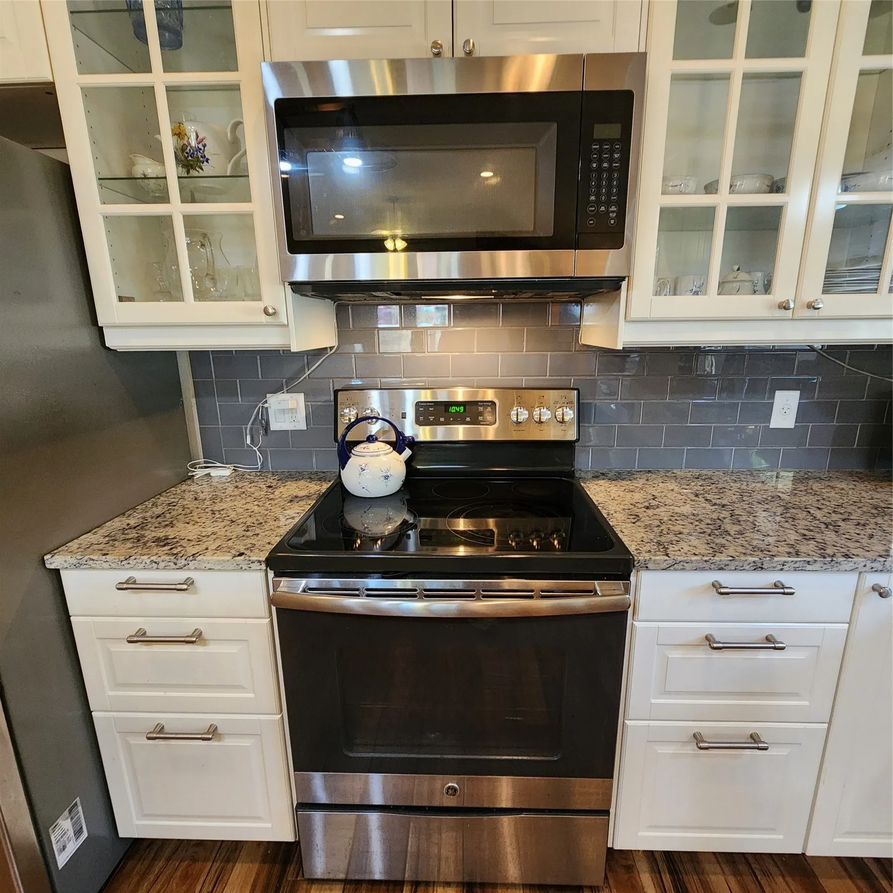 Stainless steel range and microwave oven, white shaker-style cabinetry, granite-finish countertops, and subway tile backsplash