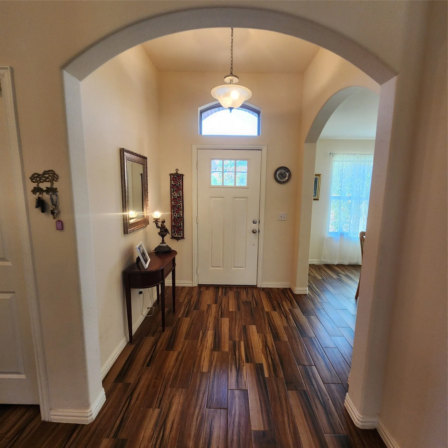 Entry foyer featuring wood-finish flooring, an arched entryway, a transom window, and a paneled entry door with decorative glass inserts