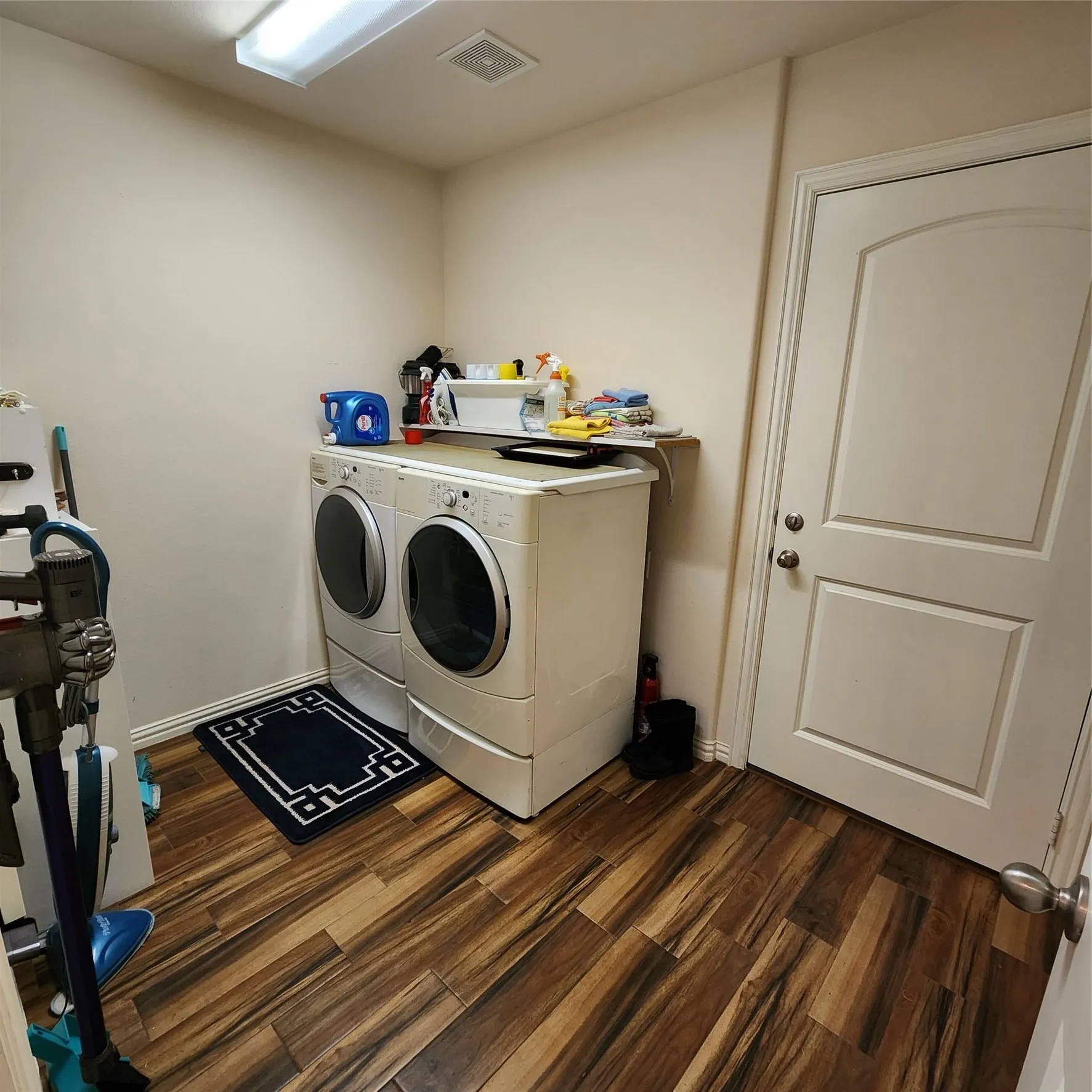 Laundry area featuring wood-finish flooring, a neutral wall color, and a built-in shelf
