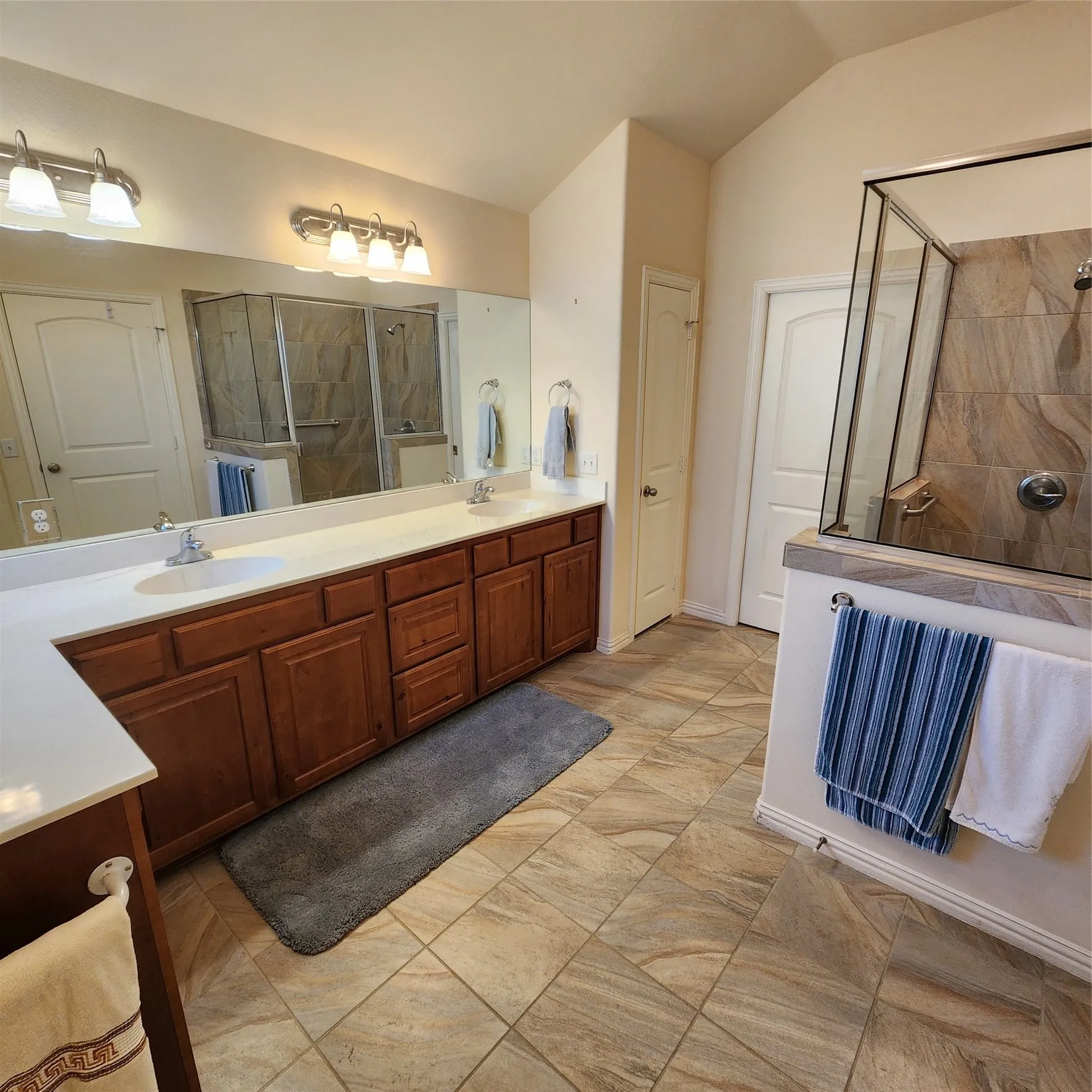 Double vanity with white countertops, wood-finish cabinetry, and an expansive mirror