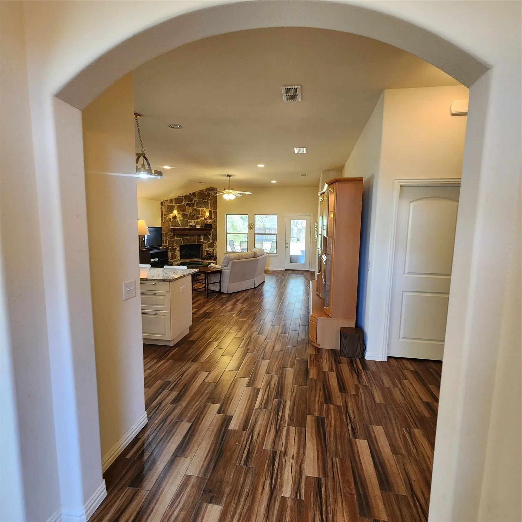 Arched doorway leading to a living area featuring wood-finish flooring, a vaulted ceiling, a stone fireplace, and multiple windows