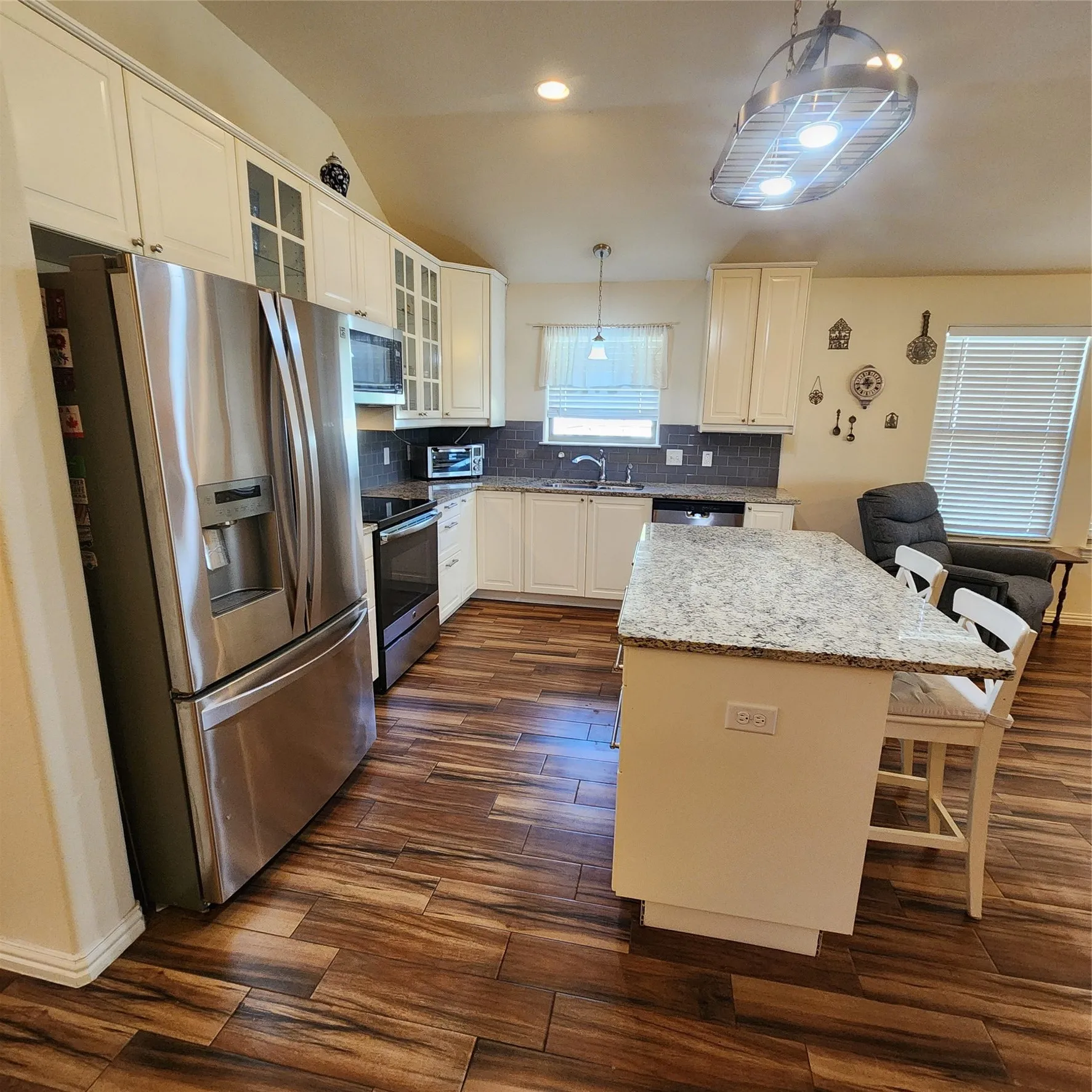 Wood-finish flooring, white cabinetry, stainless steel appliances, granite countertops, and a tile backsplash