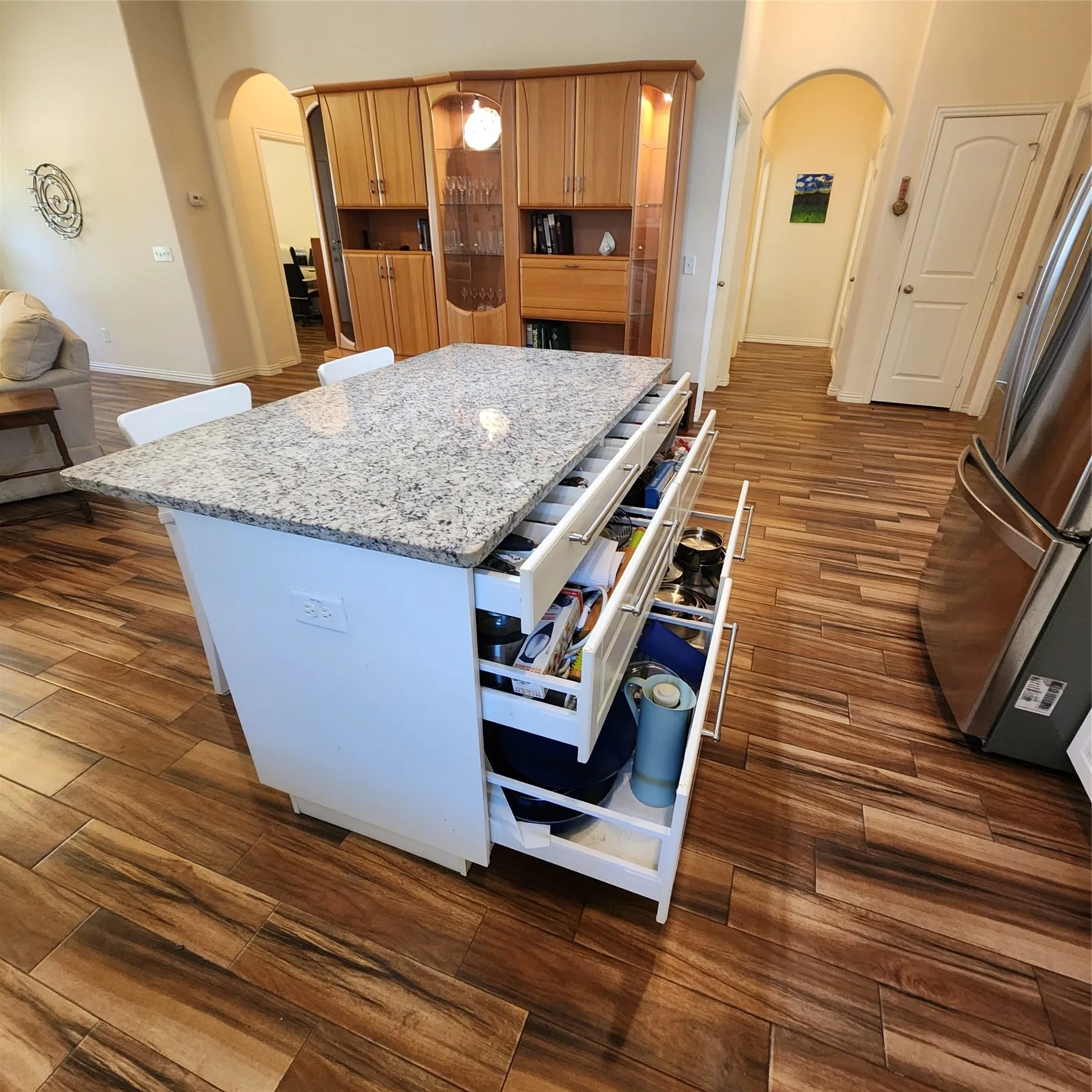 Kitchen island with a light-toned countertop, wood-finish flooring, built-in wooden cabinetry with glass inserts, and stainless steel appliances