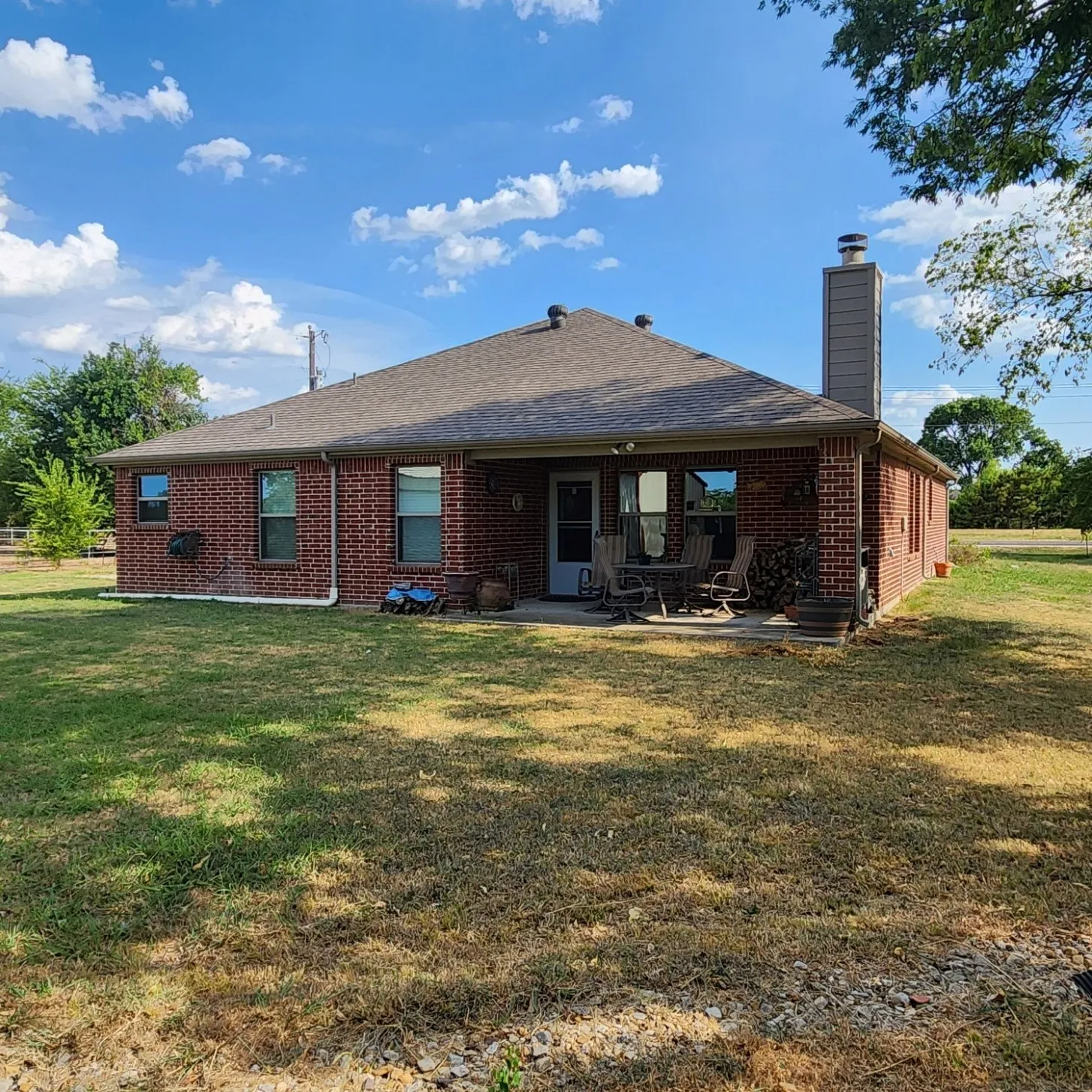 Brick exterior with a large covered patio, composite shingle roof, and a chimney