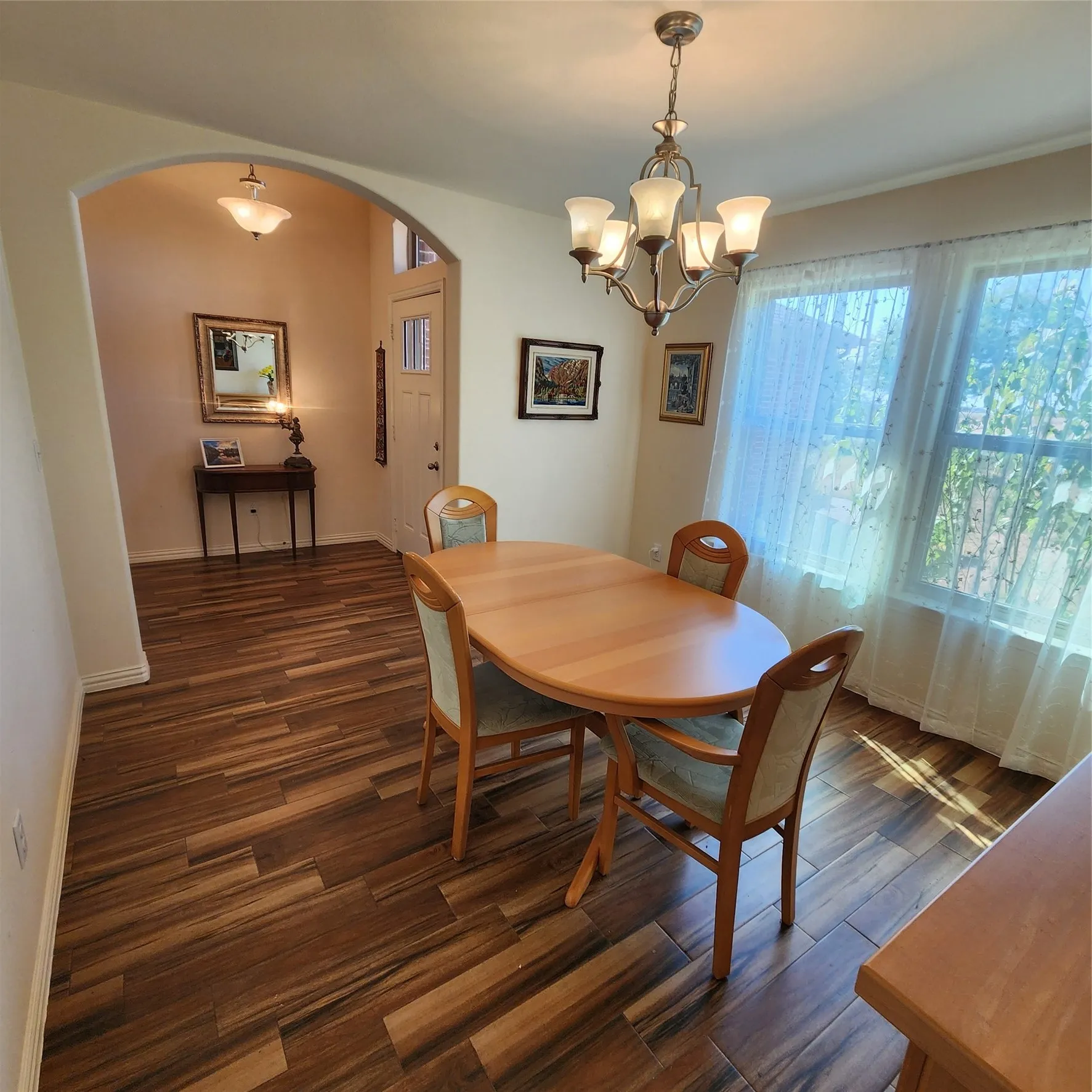Wood-finish flooring throughout, arched entryway, window with natural light, and a built-in ceiling light fixture