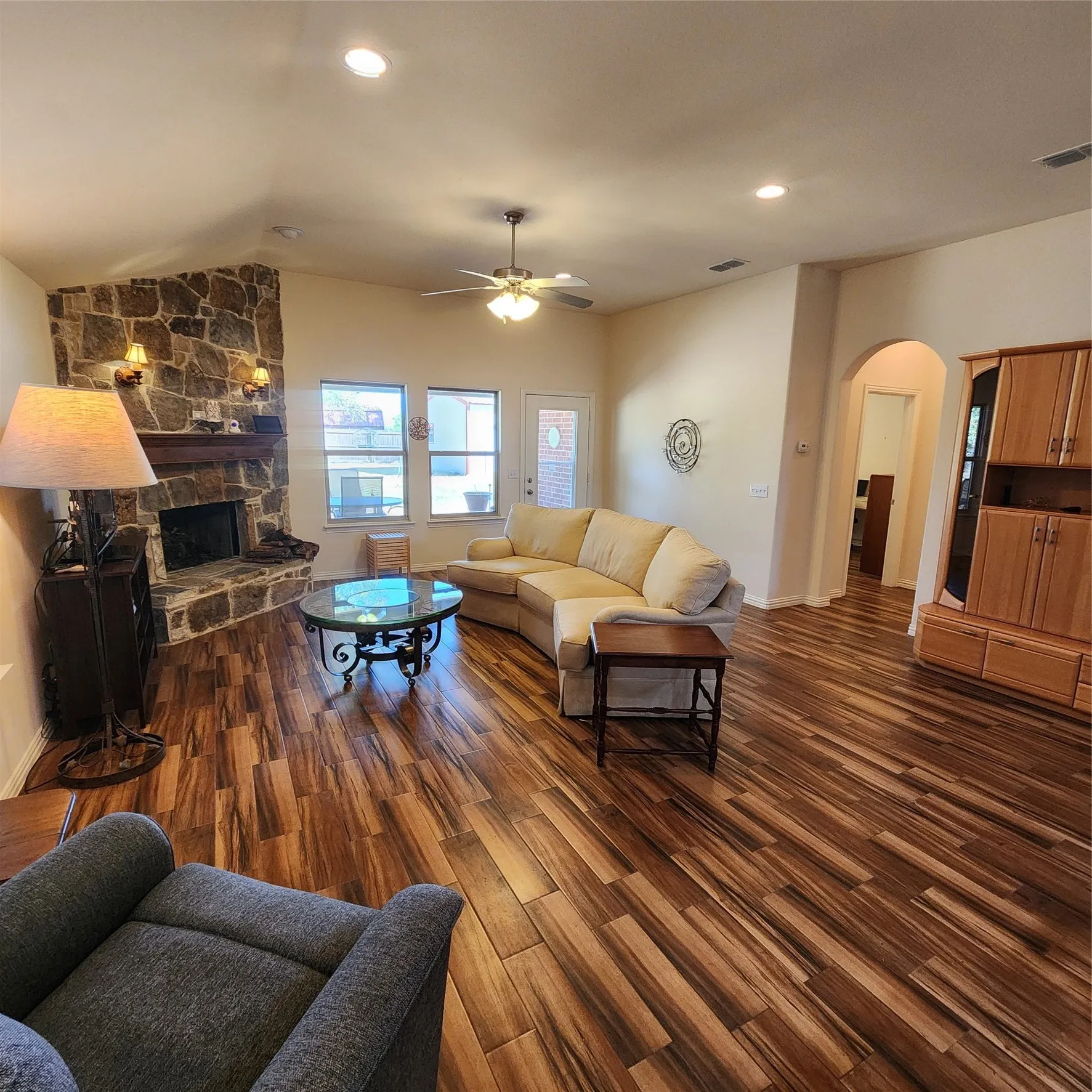 Vaulted ceiling, stone-clad fireplace with wood mantle, wood-finish flooring, recessed lighting, and a ceiling fan