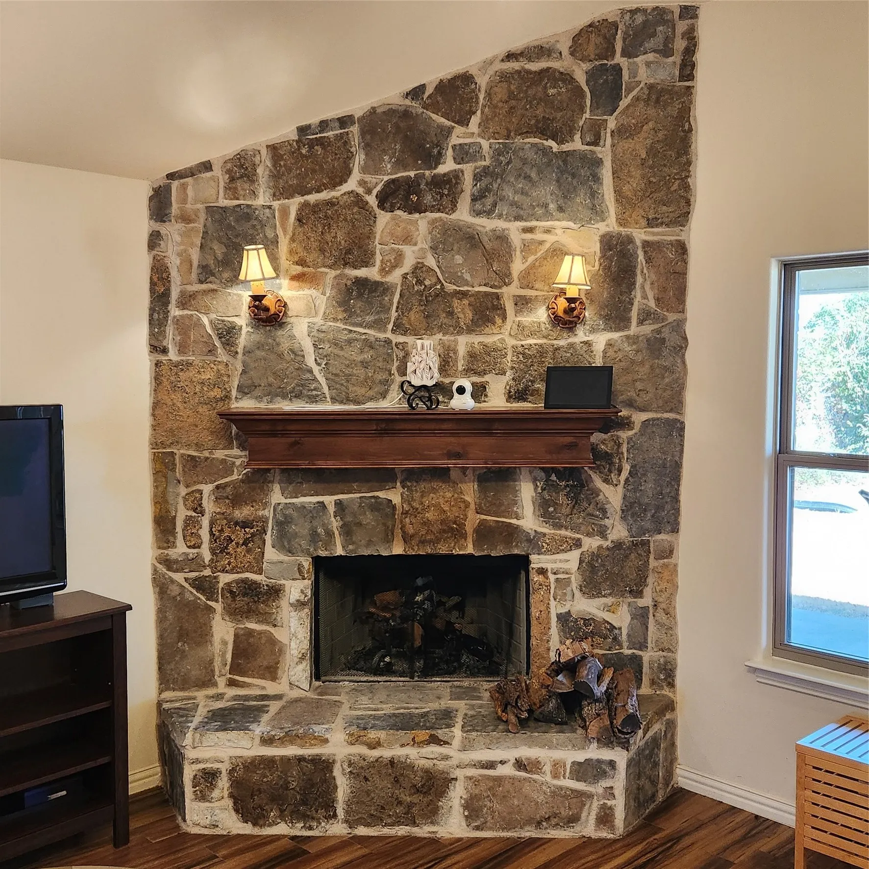 Stone-clad fireplace featuring a wood mantel, integrated sconce lighting, and a firebox with a grate