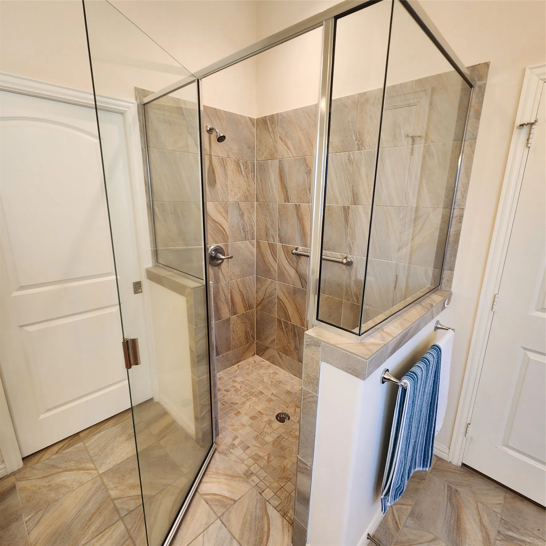 Glass-enclosed shower with a tiled surround, integrated grab bars, and a complementary mosaic tile shower floor