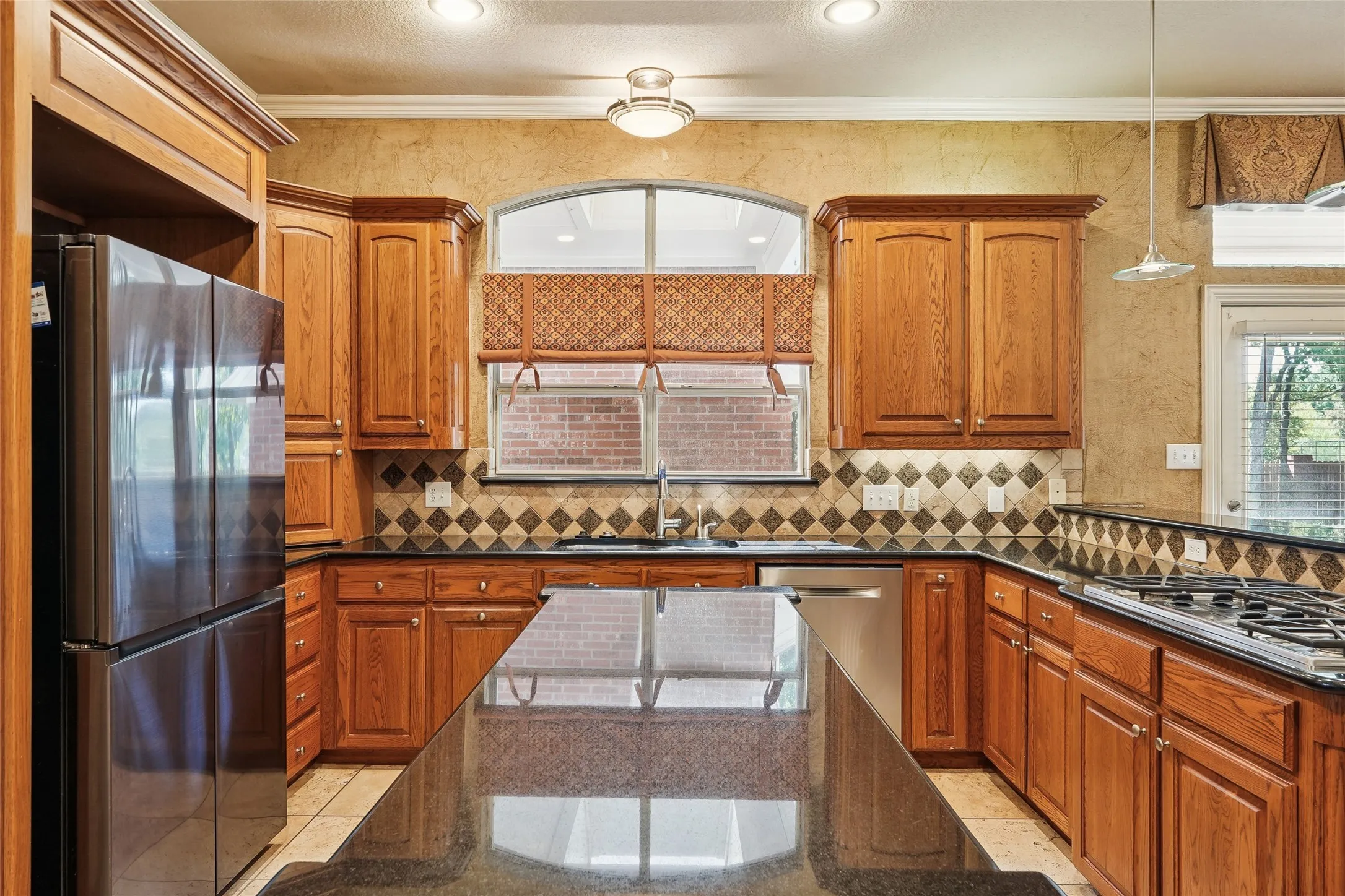 Custom wood cabinetry, stainless steel refrigerator, black gas cooktop, tile flooring, and dark countertops