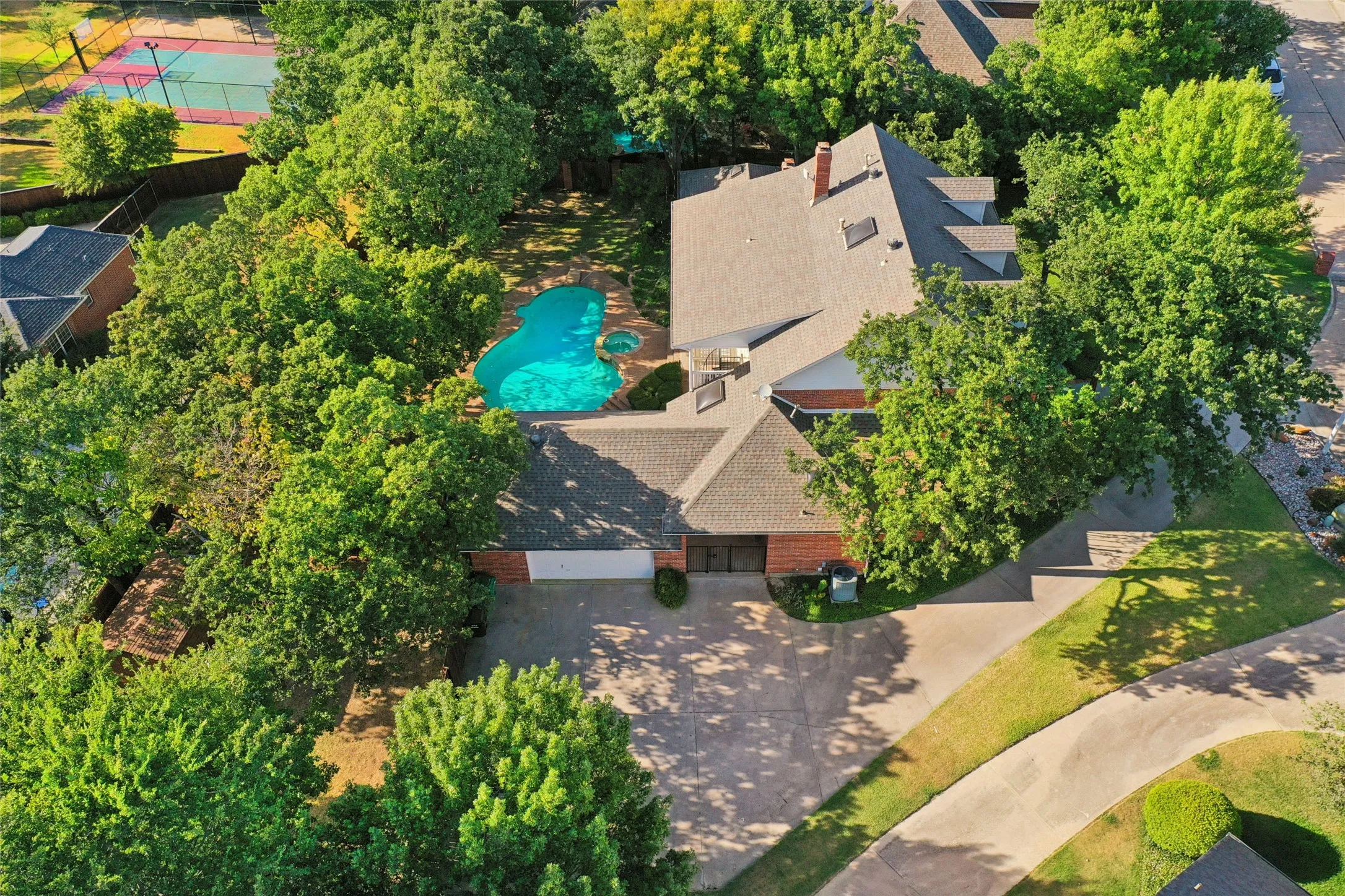 Expansive lot featuring a curvilinear swimming pool, mature tree canopy, multi-level shingle roofing, and a concrete driveway