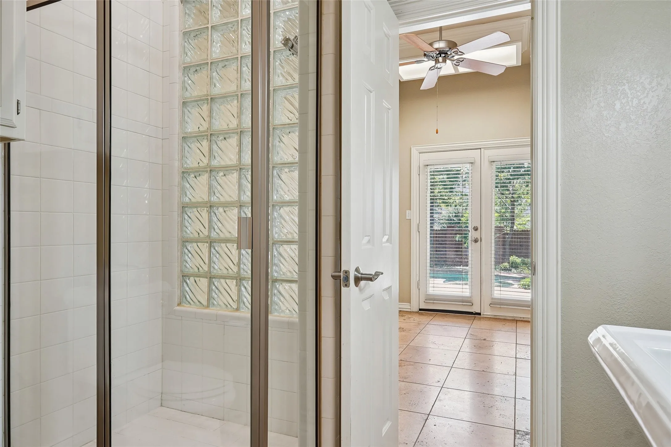 Tiled shower with glass block accent, glass shower enclosure, double French doors, tile flooring, and ceiling fan