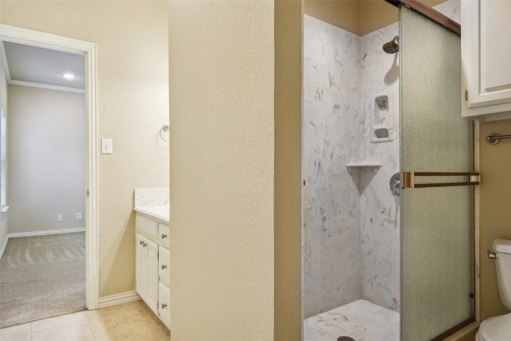 White vanity with a solid surface countertop, glass shower enclosure with a sliding door, and a white shower surround featuring an integrated corner shelf