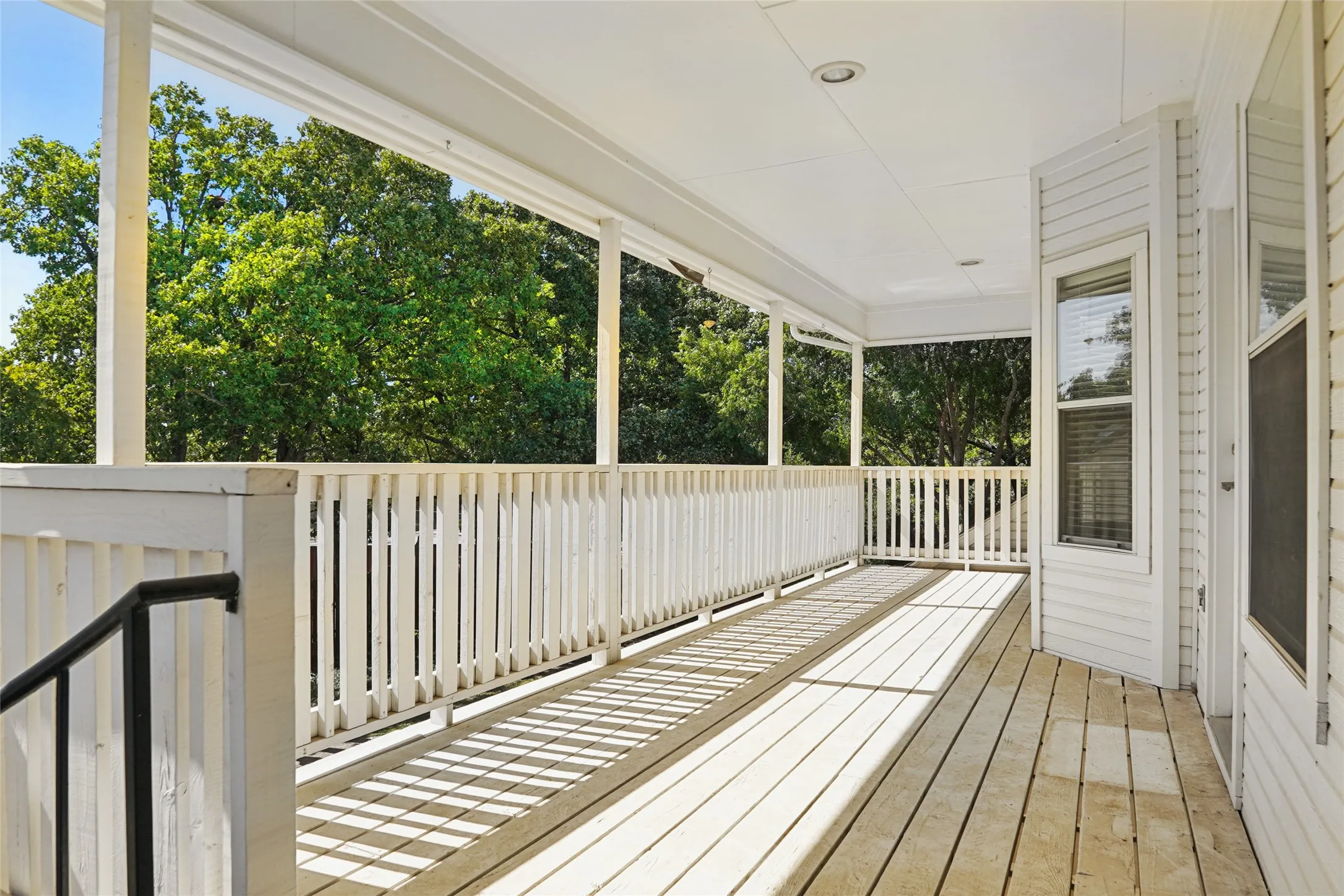 Expansive covered balcony with wood-finish flooring, white railing, and exterior wall siding
