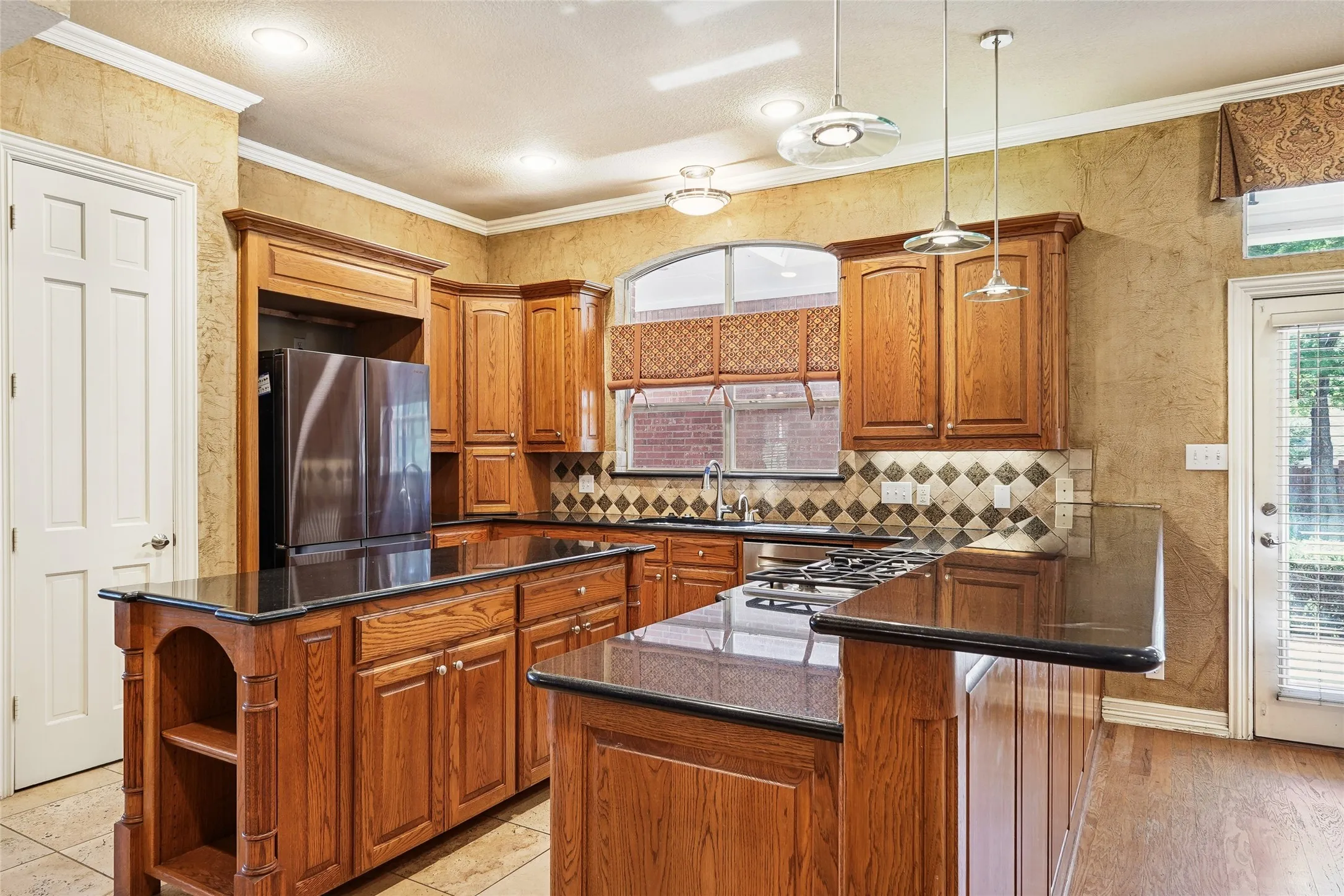 Wood cabinetry, black countertops, tile backsplash, built-in gas range, and recessed lighting