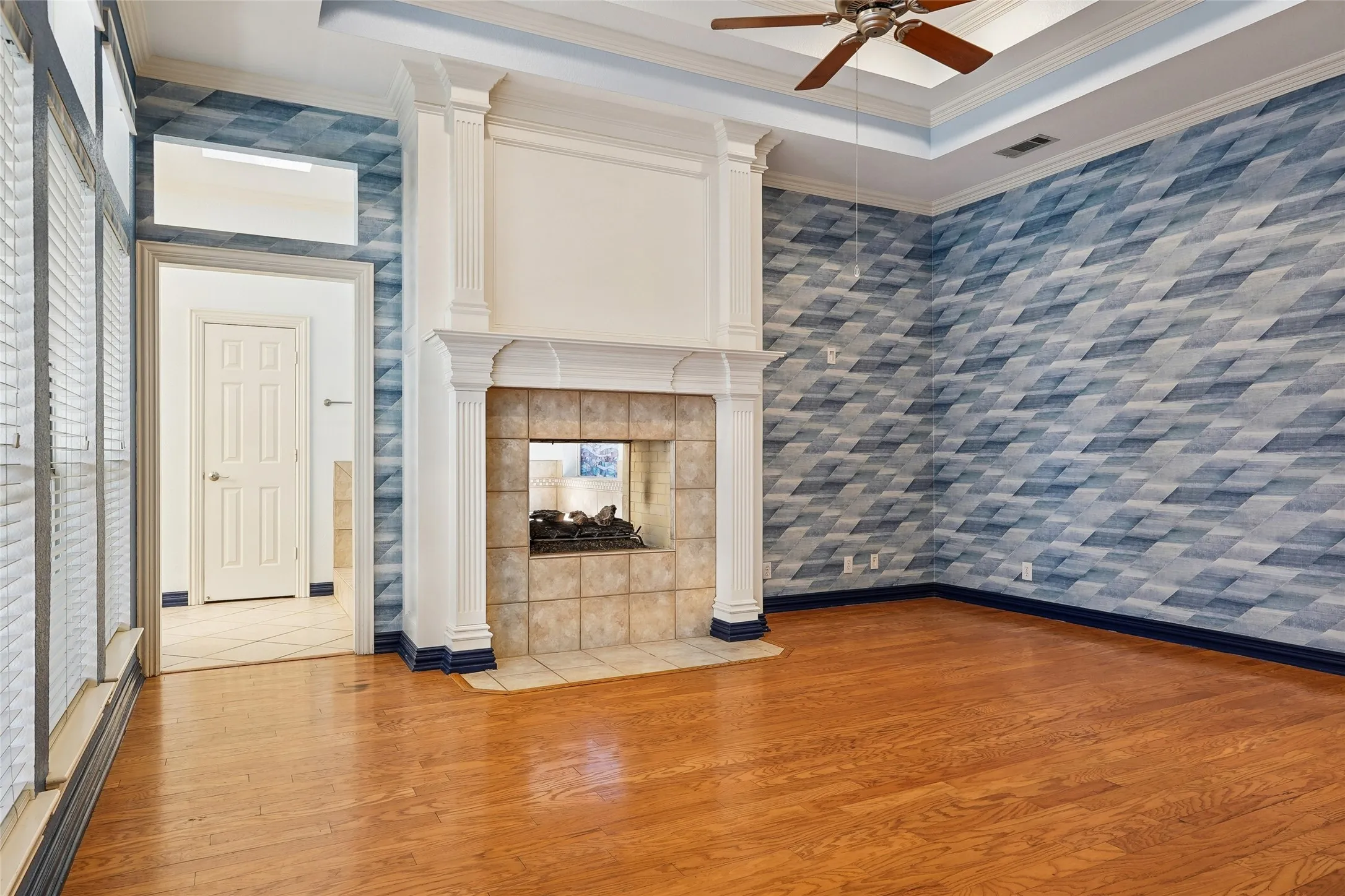 Hardwood flooring, fireplace with tile surround, decorative accent wall, tray ceiling, and ceiling fan