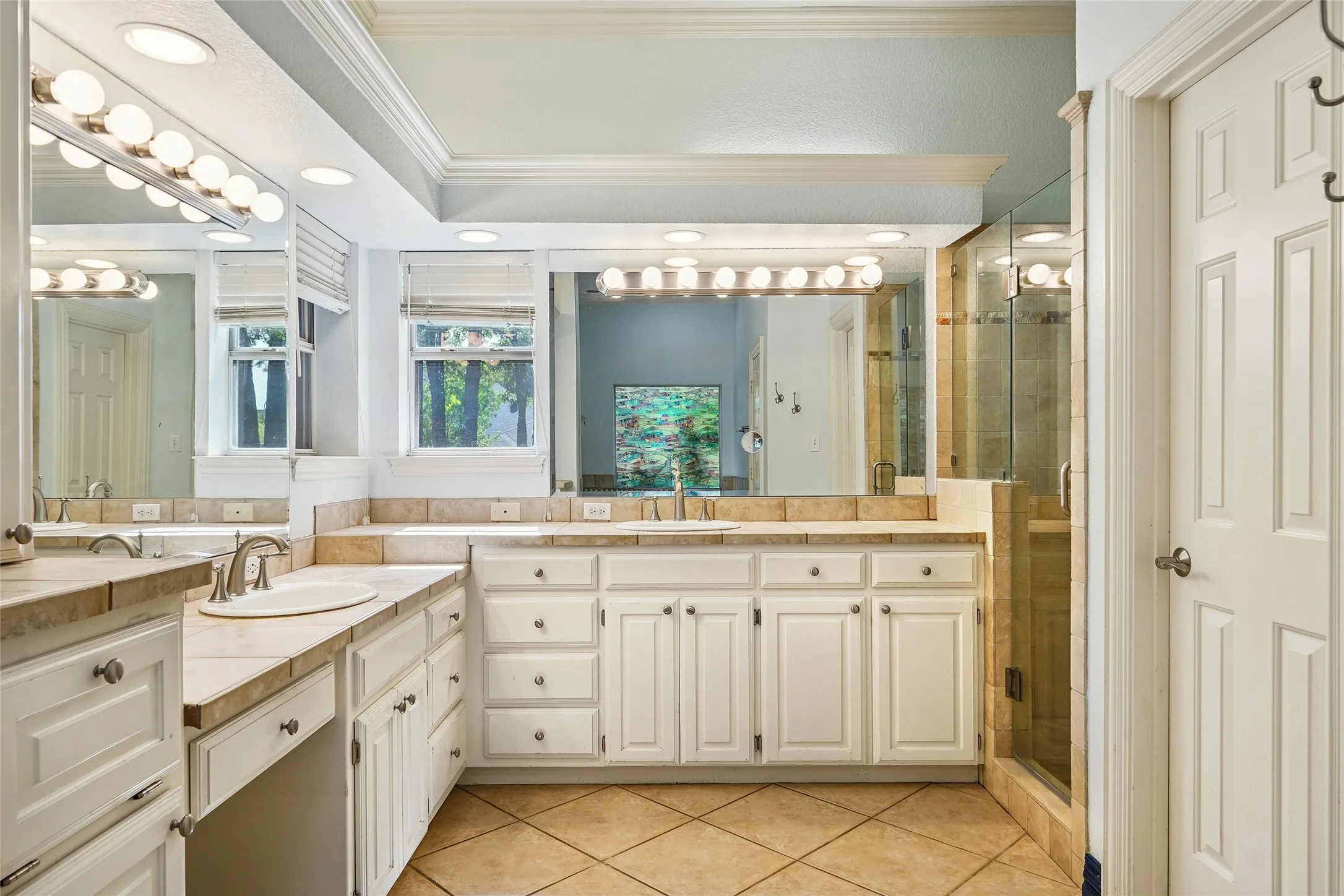 Dual vanity with undermount sinks, tile countertops, white cabinetry, and a glass-enclosed shower