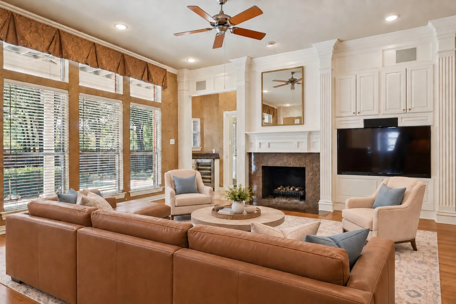 Large windows with horizontal blinds, a fireplace with a stone surround, built-in cabinetry, and hardwood flooring