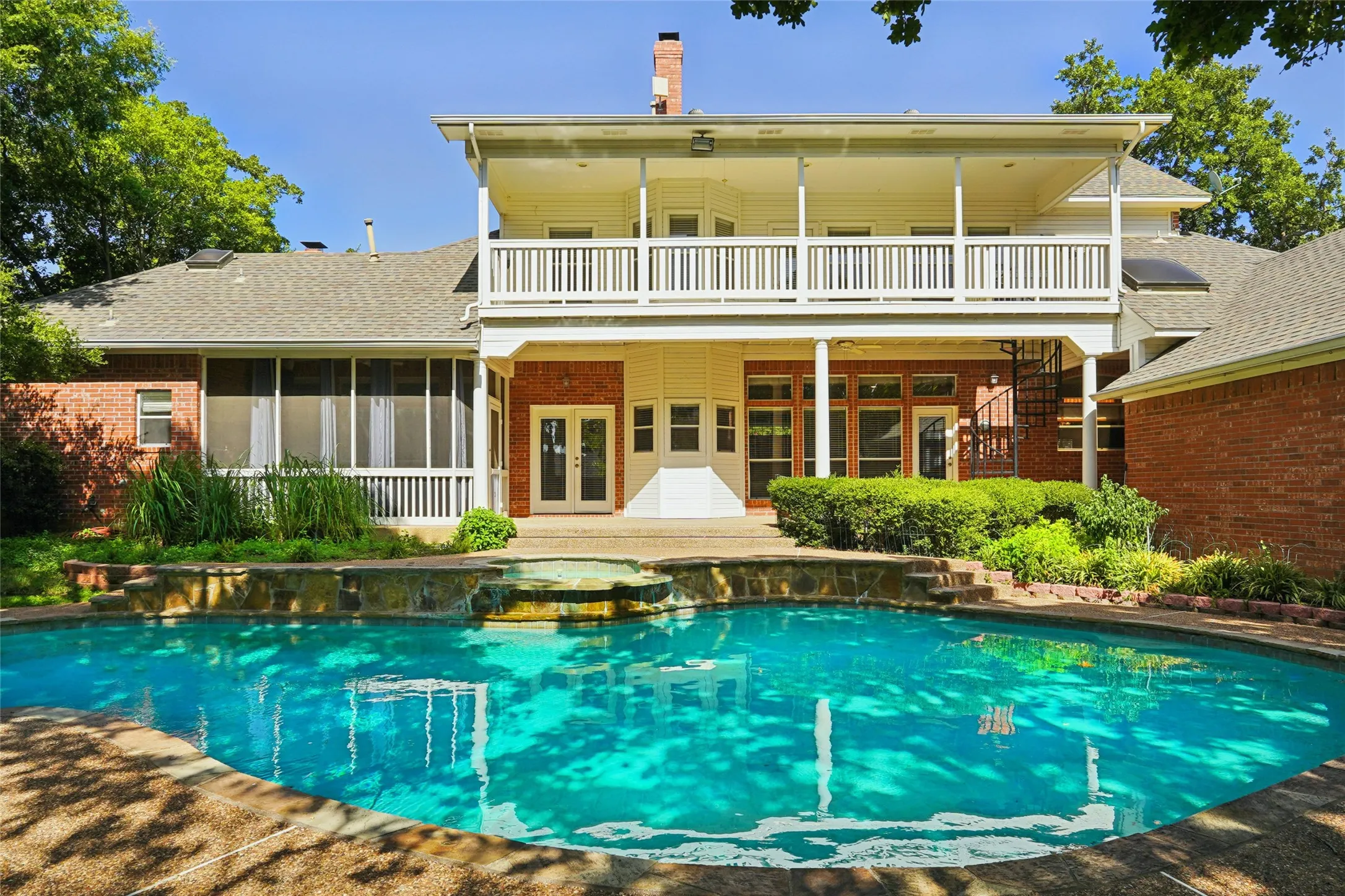 In-ground swimming pool with an integrated spa, a two-story exterior with a second-story balcony, a screened-in porch, a spiral staircase, and a brick facade