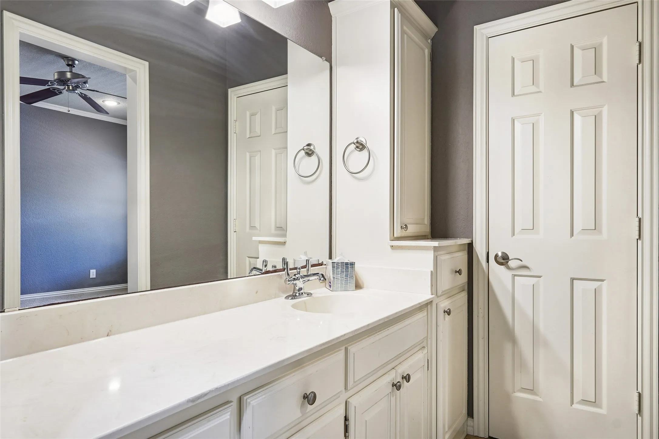 White vanity with integrated sink, polished chrome faucet, white paneled doors, and vanity lighting