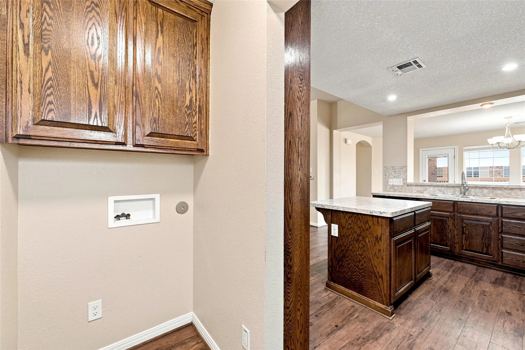 Wood-finish flooring, dark wood cabinetry, light-toned countertops, and a built-in kitchen island