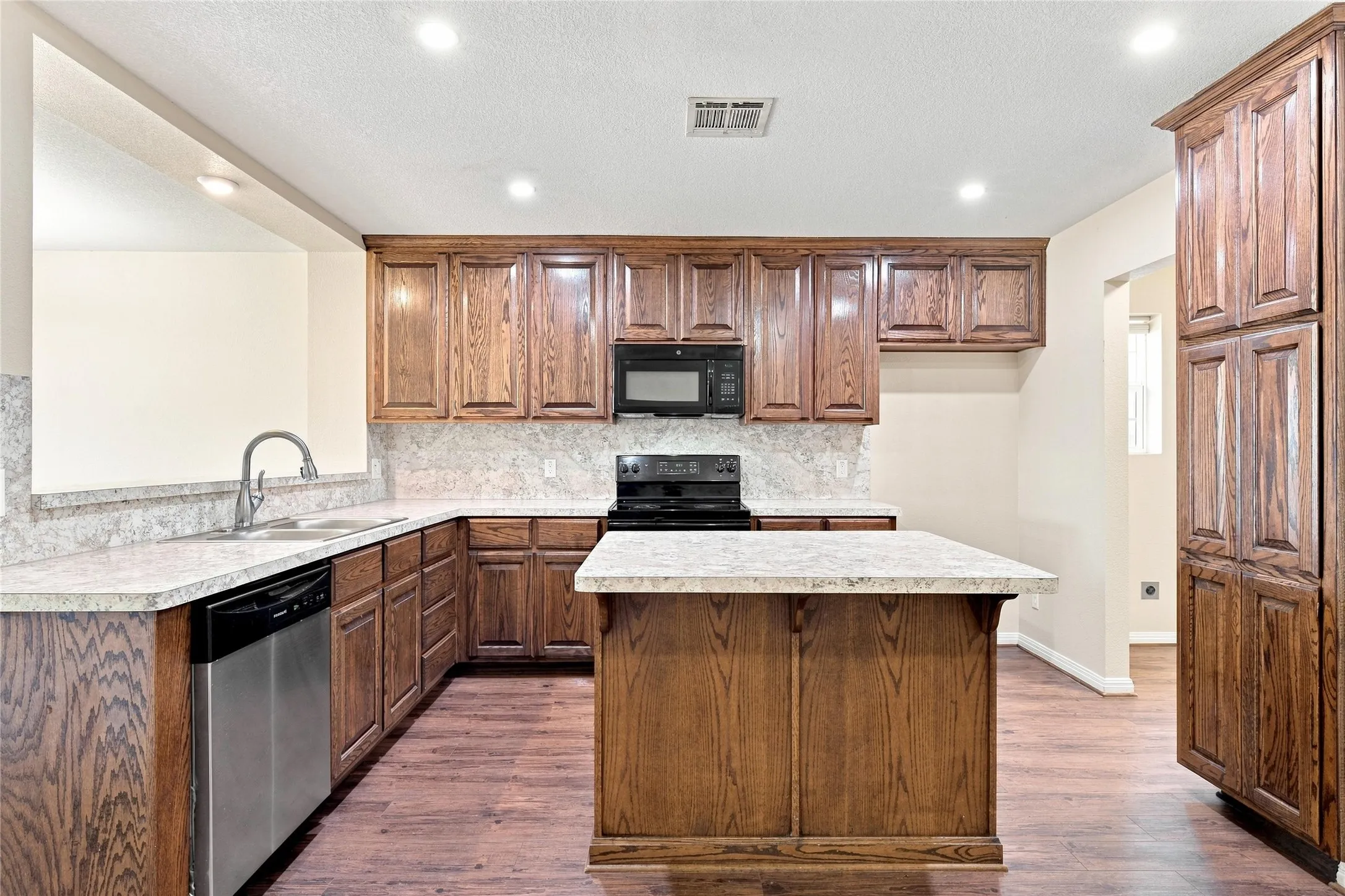 Kitchen featuring extensive wood cabinetry, L-shaped countertops, a kitchen island, integrated stainless steel dishwasher, and recessed lighting