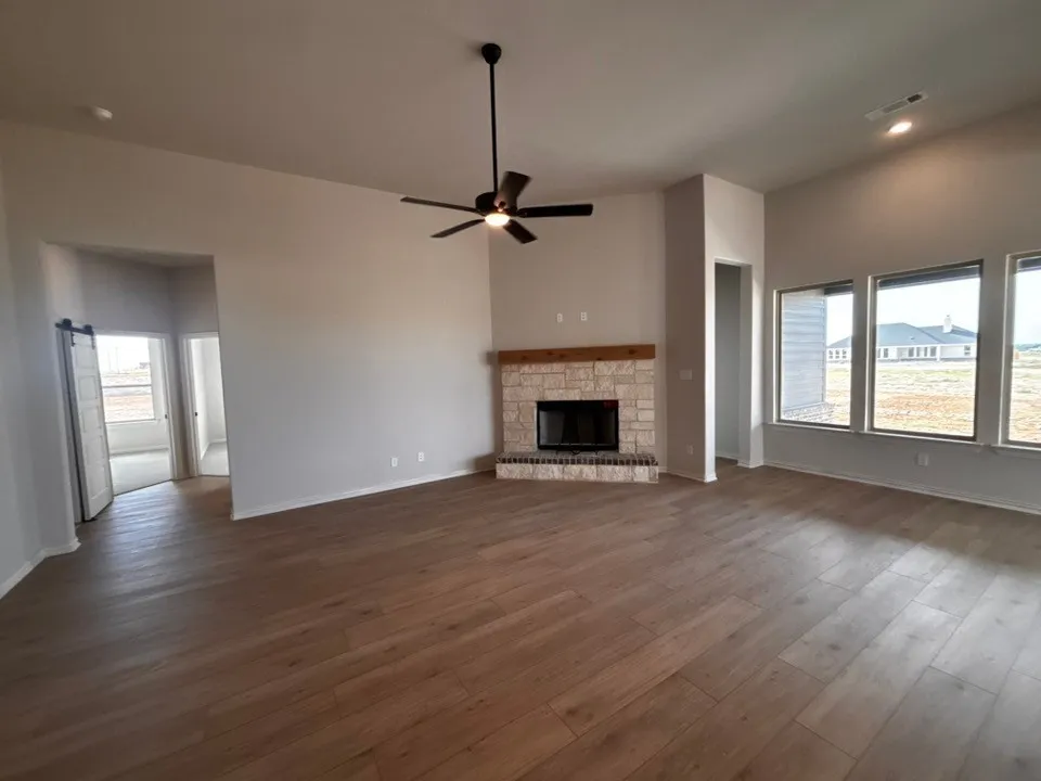 Vaulted ceilings, wood-finish flooring, stone fireplace with a wood mantle, ceiling fan, and recessed lighting