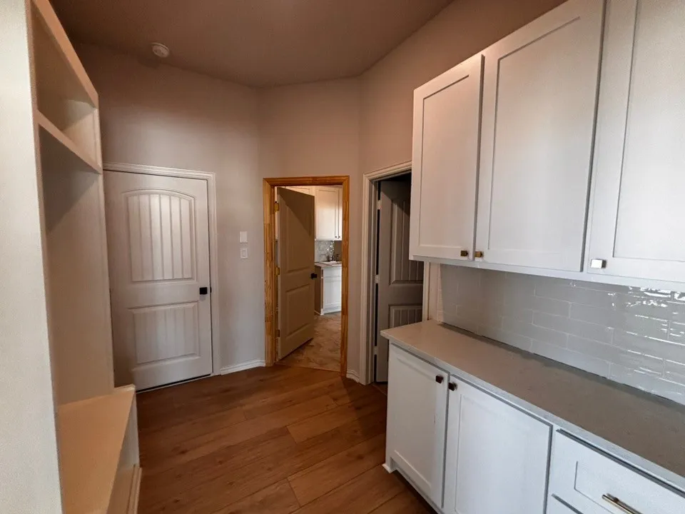 Wood-finish flooring, built-in shelving, white paneled doors, white cabinetry, and a subway tile backsplash