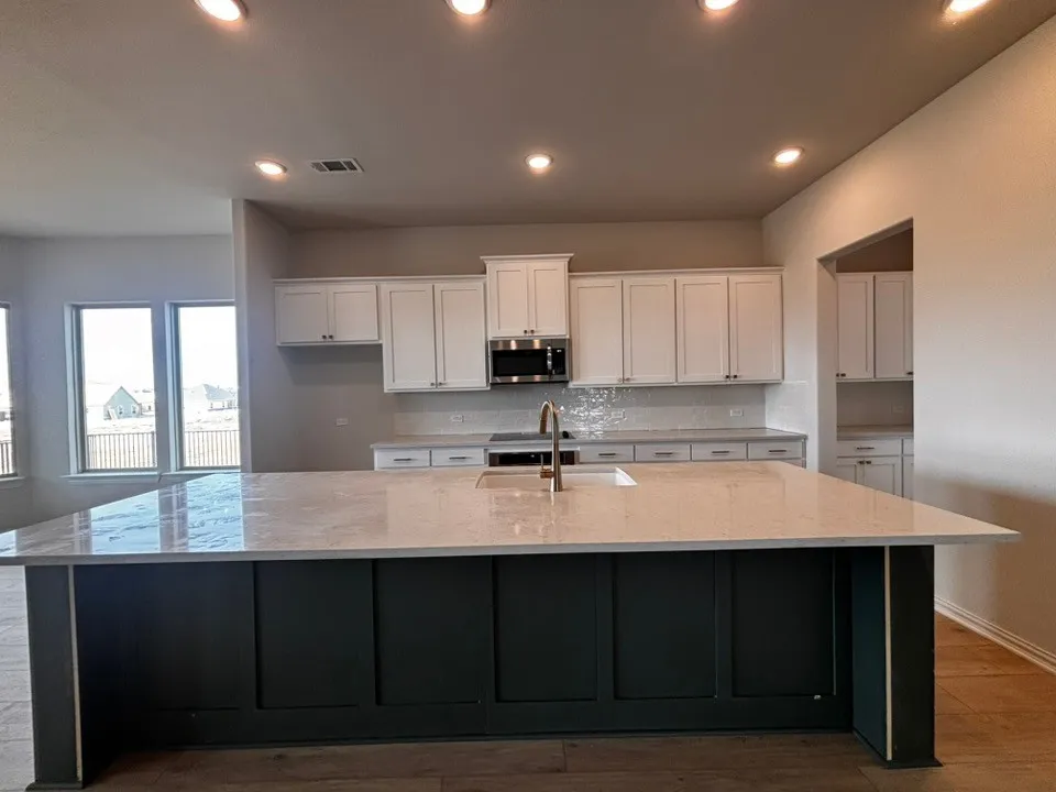 Spacious kitchen featuring a large island with a light-toned countertop, white cabinetry, a built-in microwave, and recessed lighting