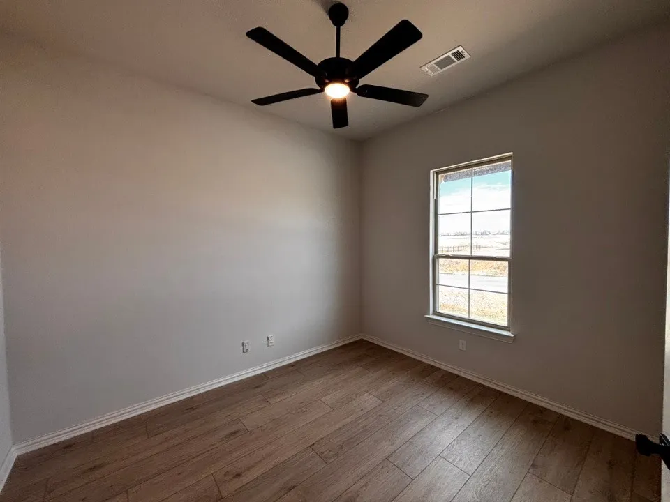 Wood-finish flooring, a ceiling fan with integrated lighting, and a window with white trim
