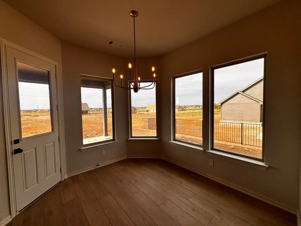 Wood-finish flooring, multiple large windows, a single light fixture, and a white door with a window pane
