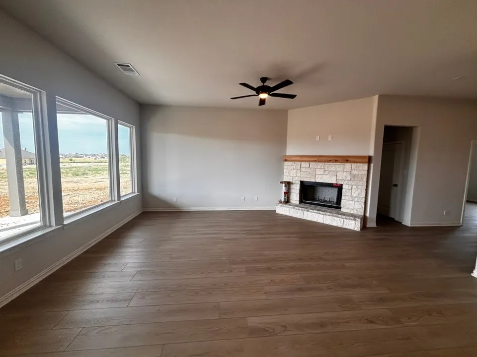 Wood-finish flooring throughout, multiple large windows, corner fireplace with stone surround and wood mantel, and ceiling fan with integrated lighting