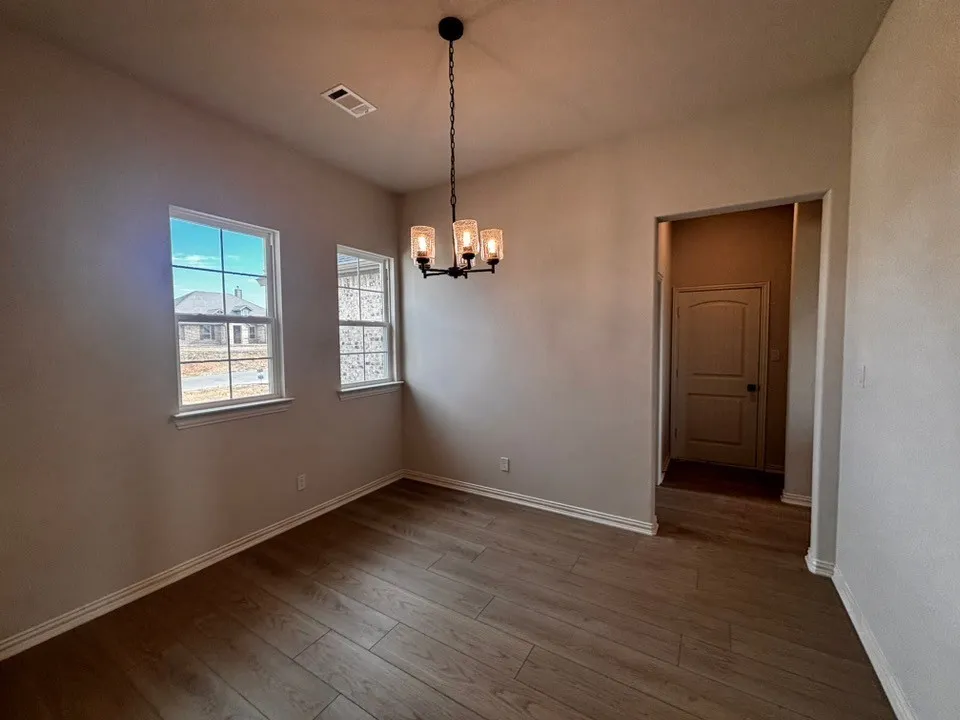 Wood-finish plank flooring, two double-hung windows, a three-light chandelier with clear glass shades, and a paneled interior door