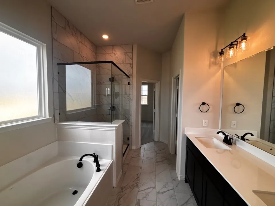 Dual vanity with undermount sinks, frameless glass shower enclosure, soaking tub with black fixtures, and patterned tile flooring